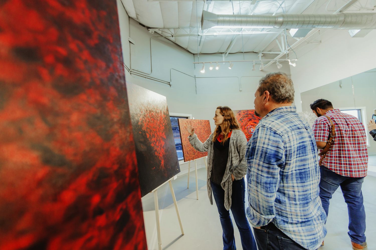 A group of people stand in front of an art installation with dramatic red lighting in a gallery space.