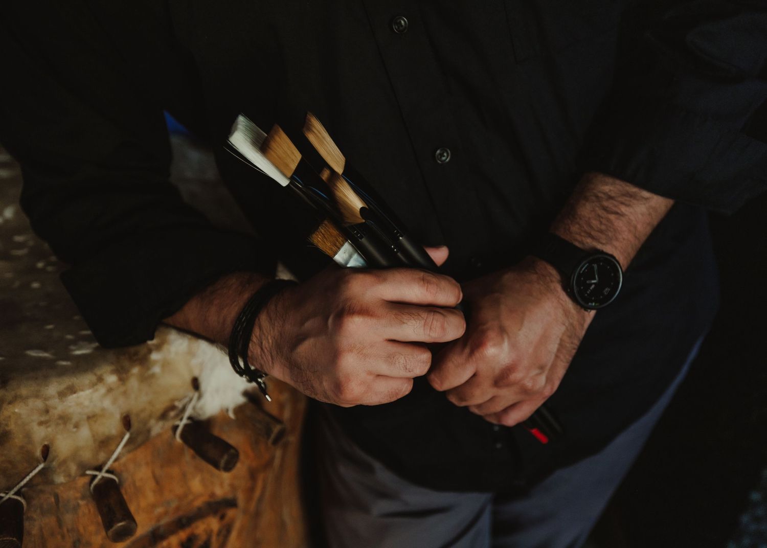Close-up view of hands holding a cigar and wearing a luxury watch against dark clothing.
