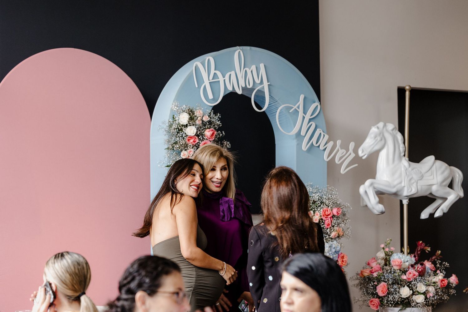 Two people share a tender embrace in front of a pink and blue wall with chic floral decorations and elegant signage.
