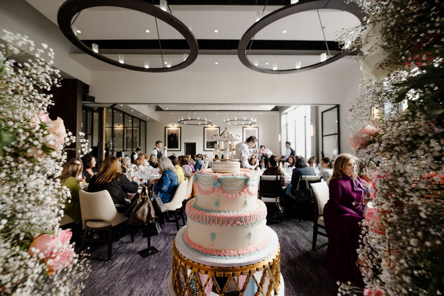 A wedding reception hall decorated with soft pink floral arrangements and pendant lights creates an elegant atmosphere.