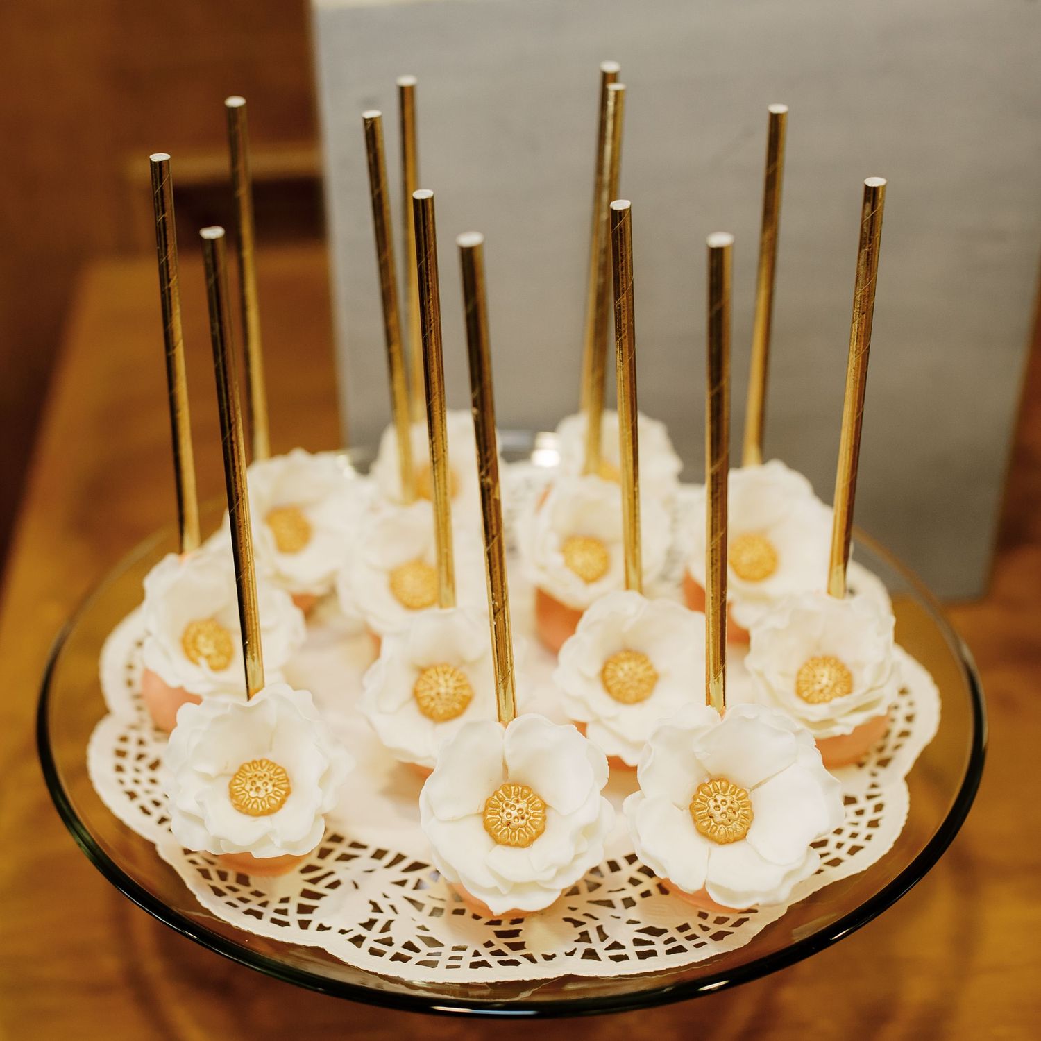 Gold cake pops decorated with white frosting arranged on a decorative doily plate.