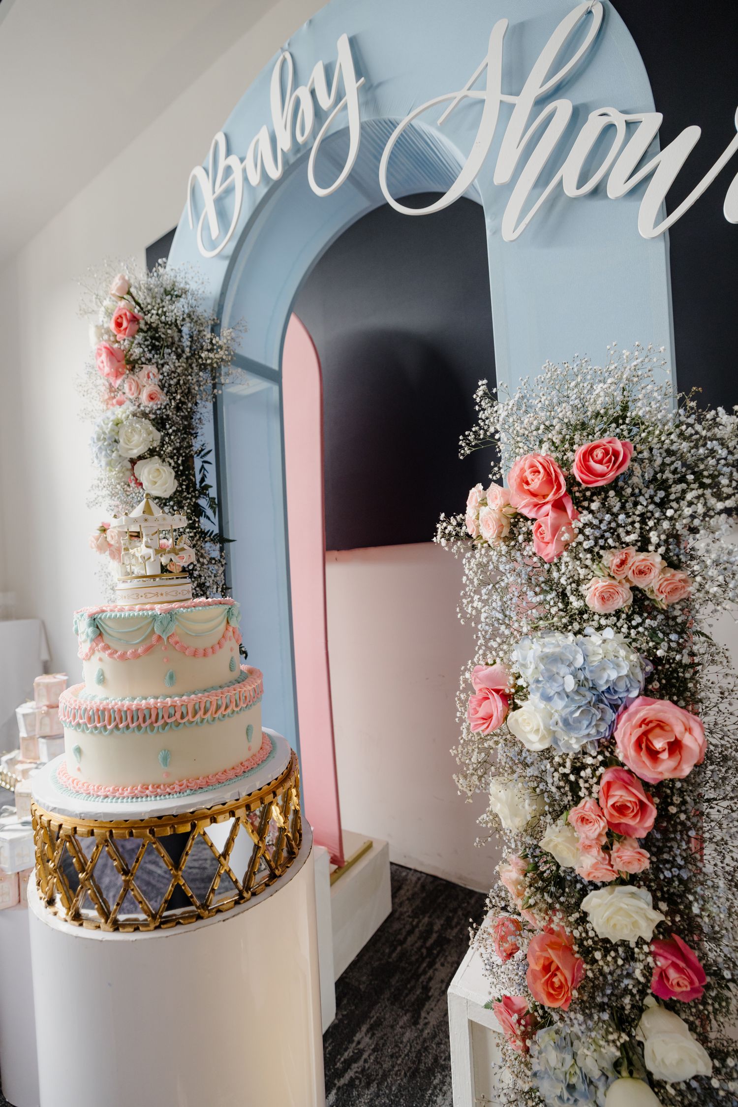 A white and pink wedding cake sits beside a pastel blue arch adorned with coral roses and baby's breath floral arrangements.