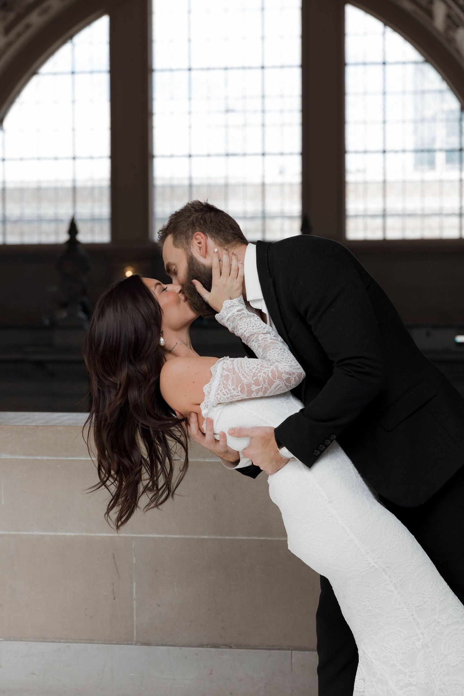 Romantic wedding photo of a couple in formal attire sharing an intimate moment in a grand indoor setting.