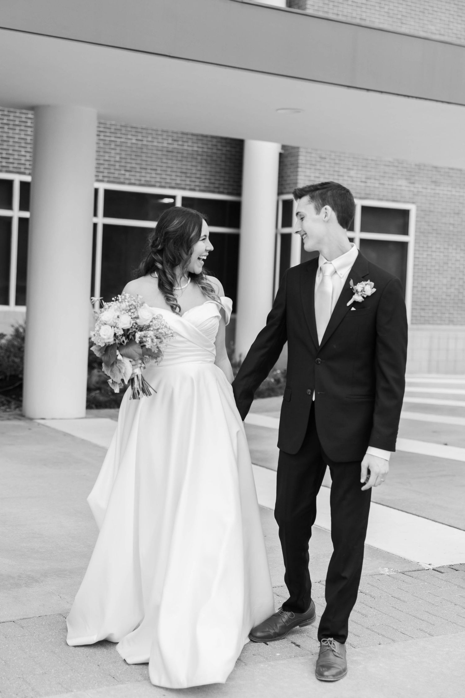 Black and white portrait of newlyweds walking together in formal wedding attire.