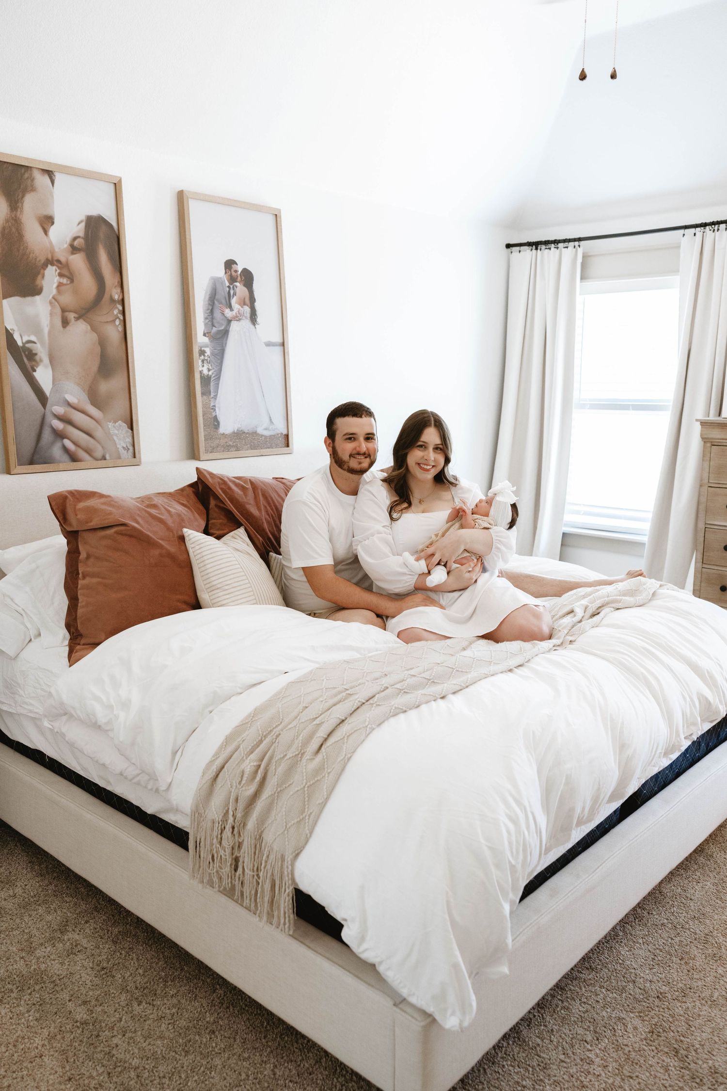 Cozy bedroom interior with white bedding, brown pillows and framed photographs on wall.