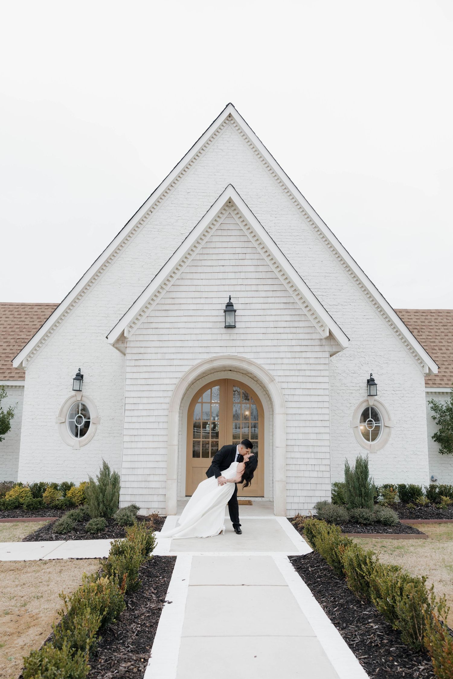White chapel with A-frame architecture and newlyweds entering through wooden door.
