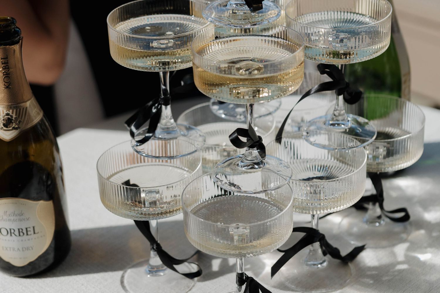 Close-up of stacked champagne coupes with black ribbon accents on white linen.