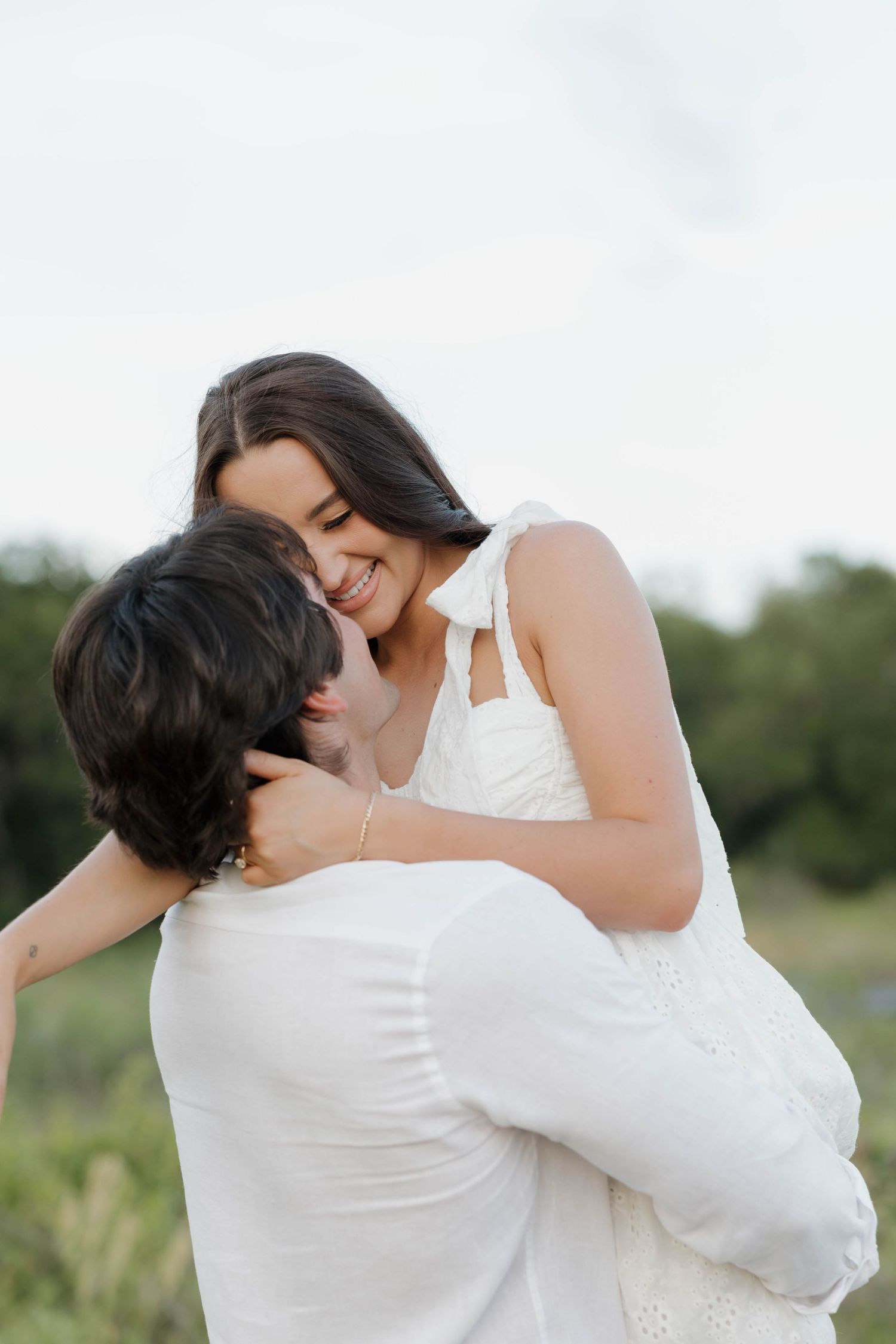 A romantic outdoor moment with a couple in white embracing against a natural backdrop.