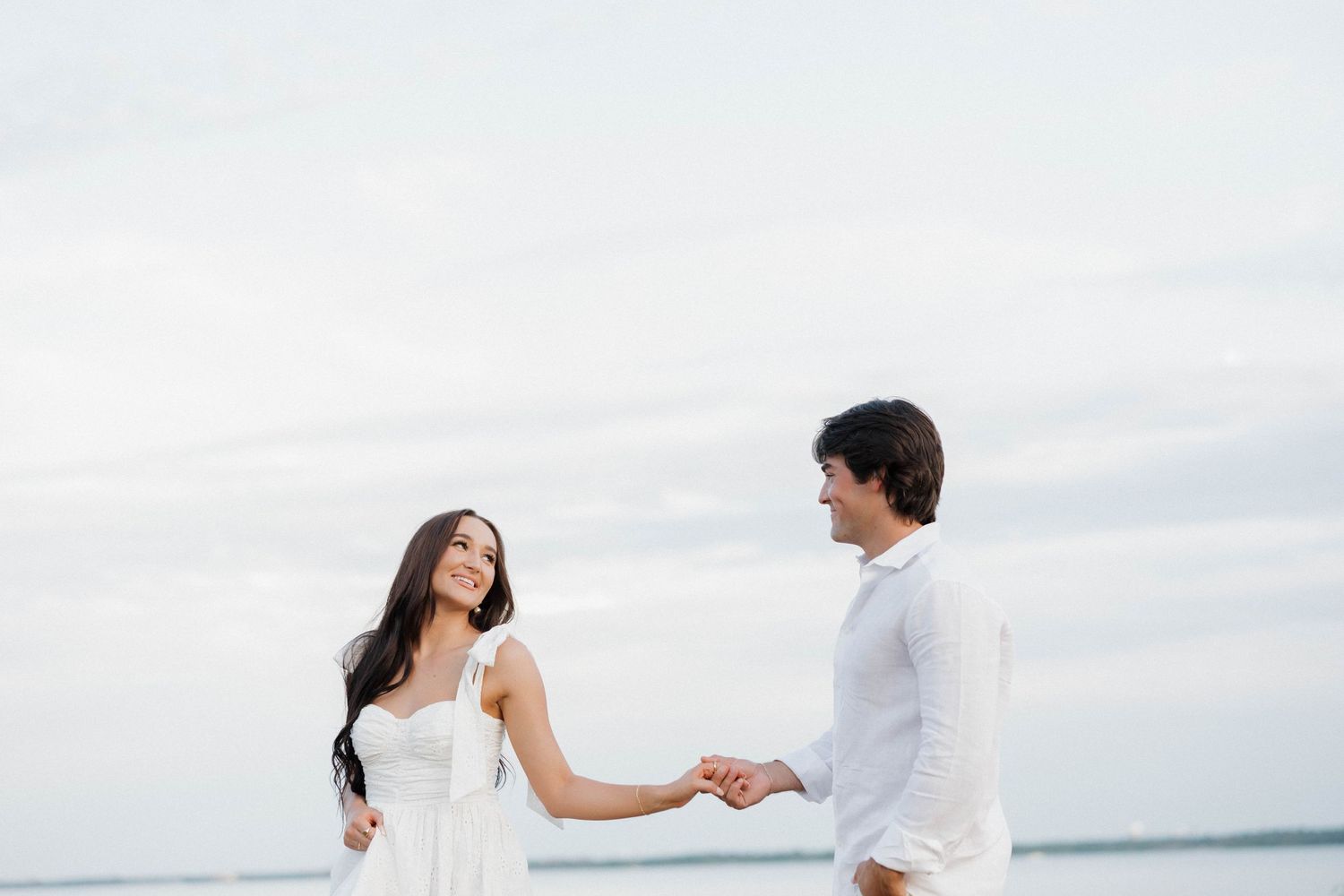 A romantic beach scene with a couple in white attire holding hands by the ocean.