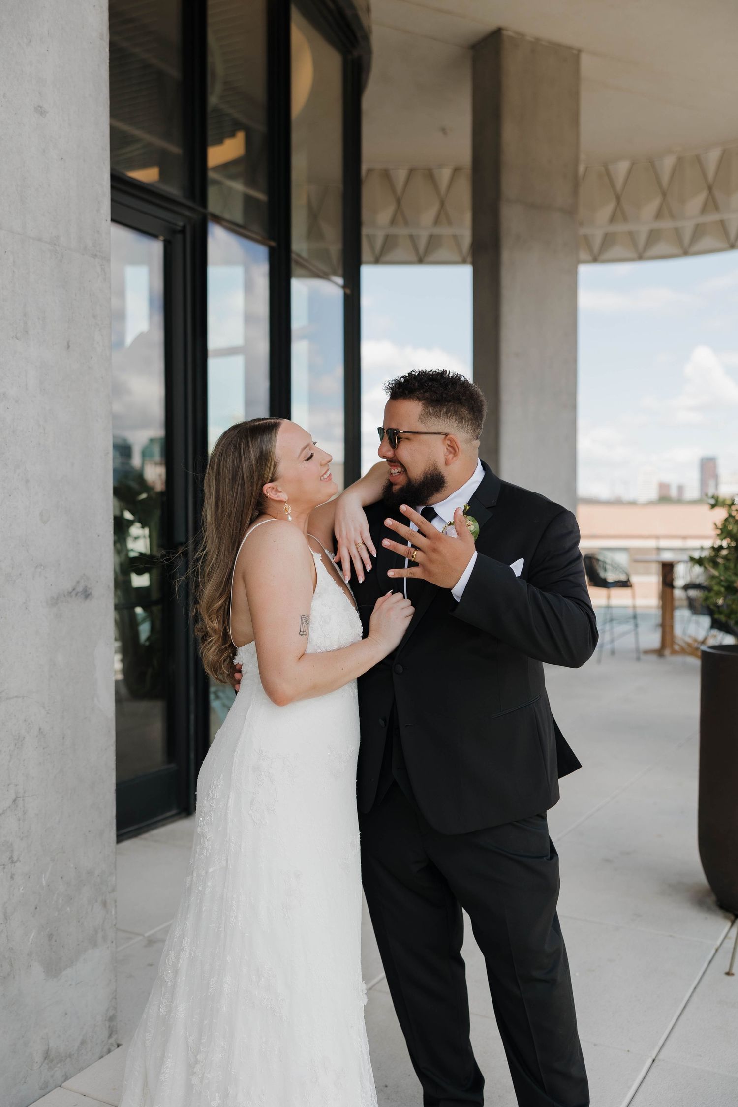 Couple sharing joyful moment on modern building terrace in formal wedding attire.