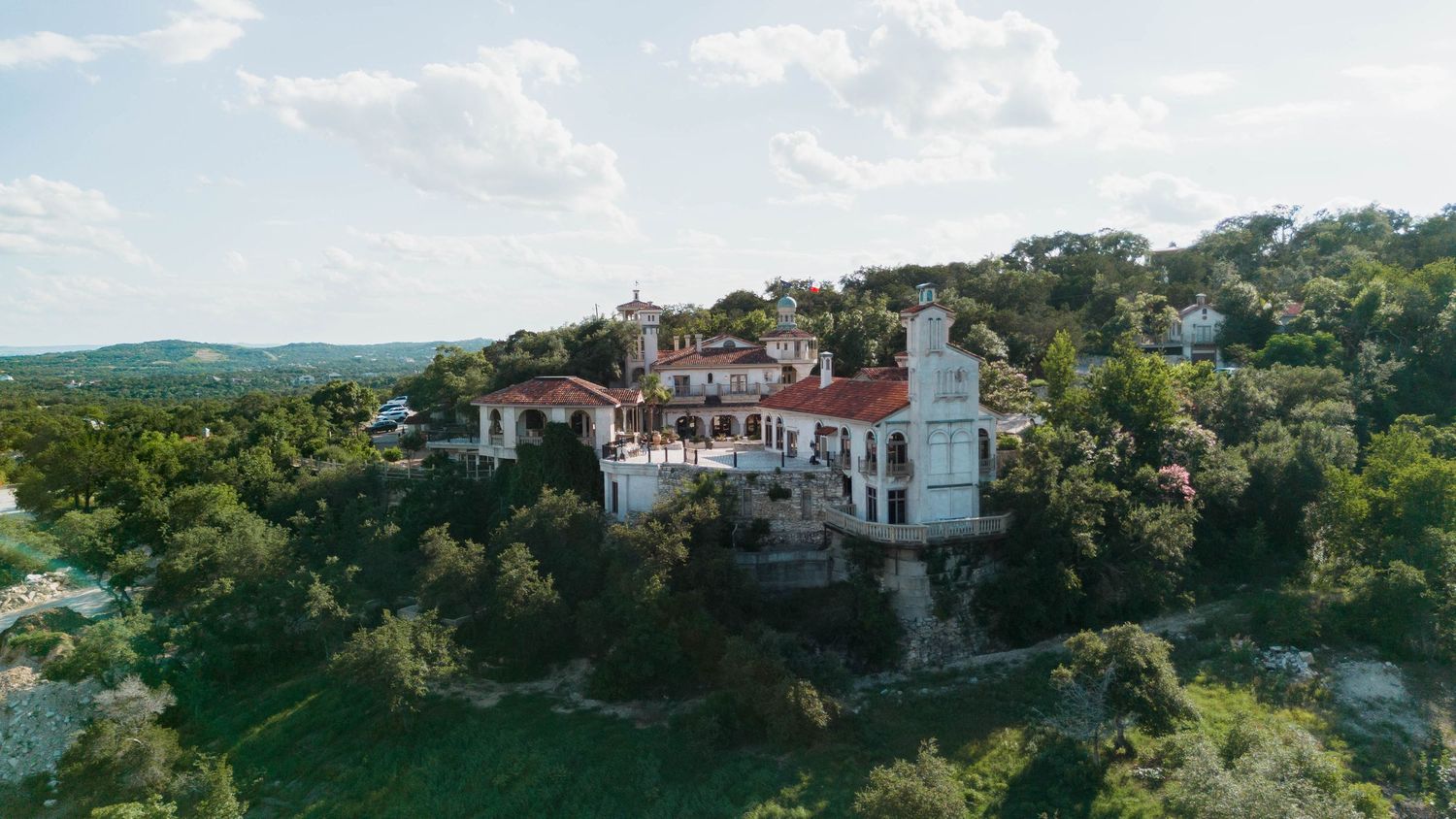 Panoramic view of an elegant white mansion with terra cotta roofs perched on a hilltop.