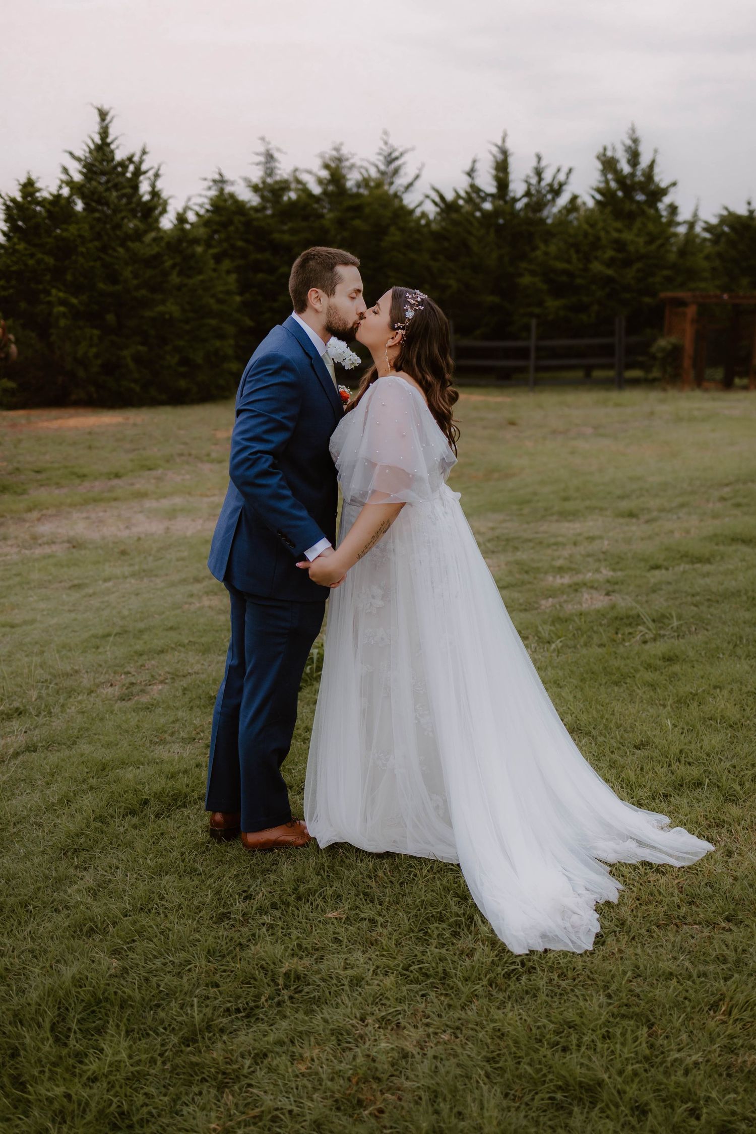 Romantic wedding portrait of couple embracing in field with evergreen trees.