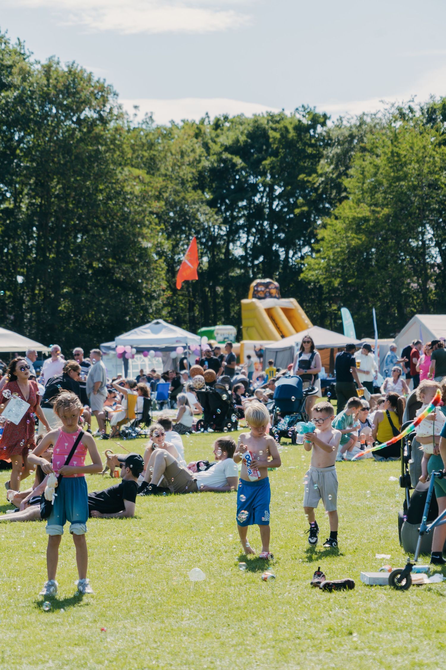 People enjoying a sunny summer festival with inflatable bounce houses, outdoor activities and families on a grassy field.