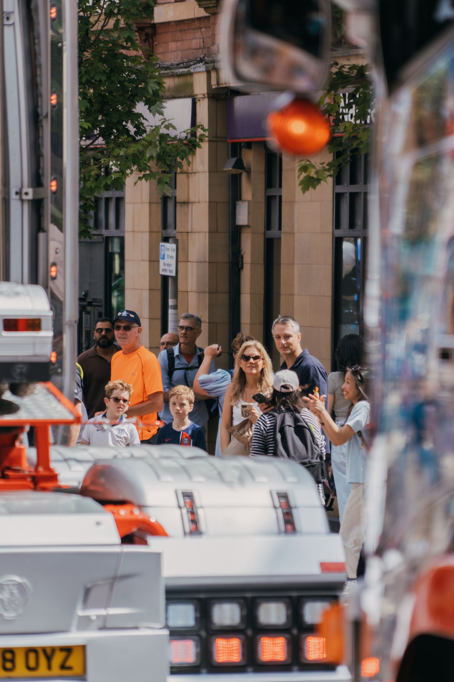 A busy urban street scene with people walking past storefronts and outdoor seating areas in a city setting.