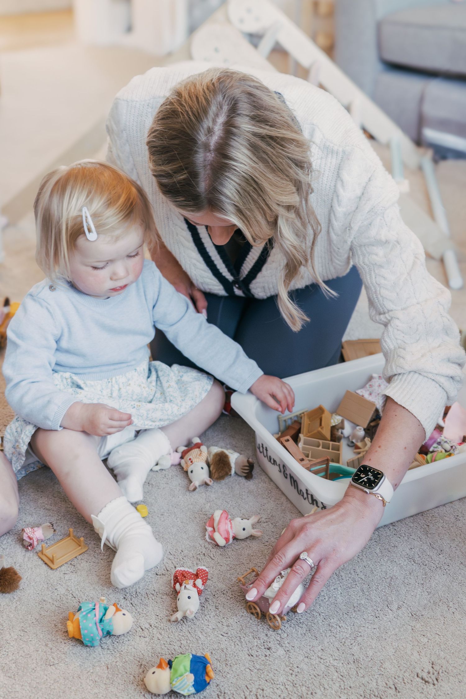 Playing with colorful toys on a carpeted floor while someone helps arrange the scattered pieces.