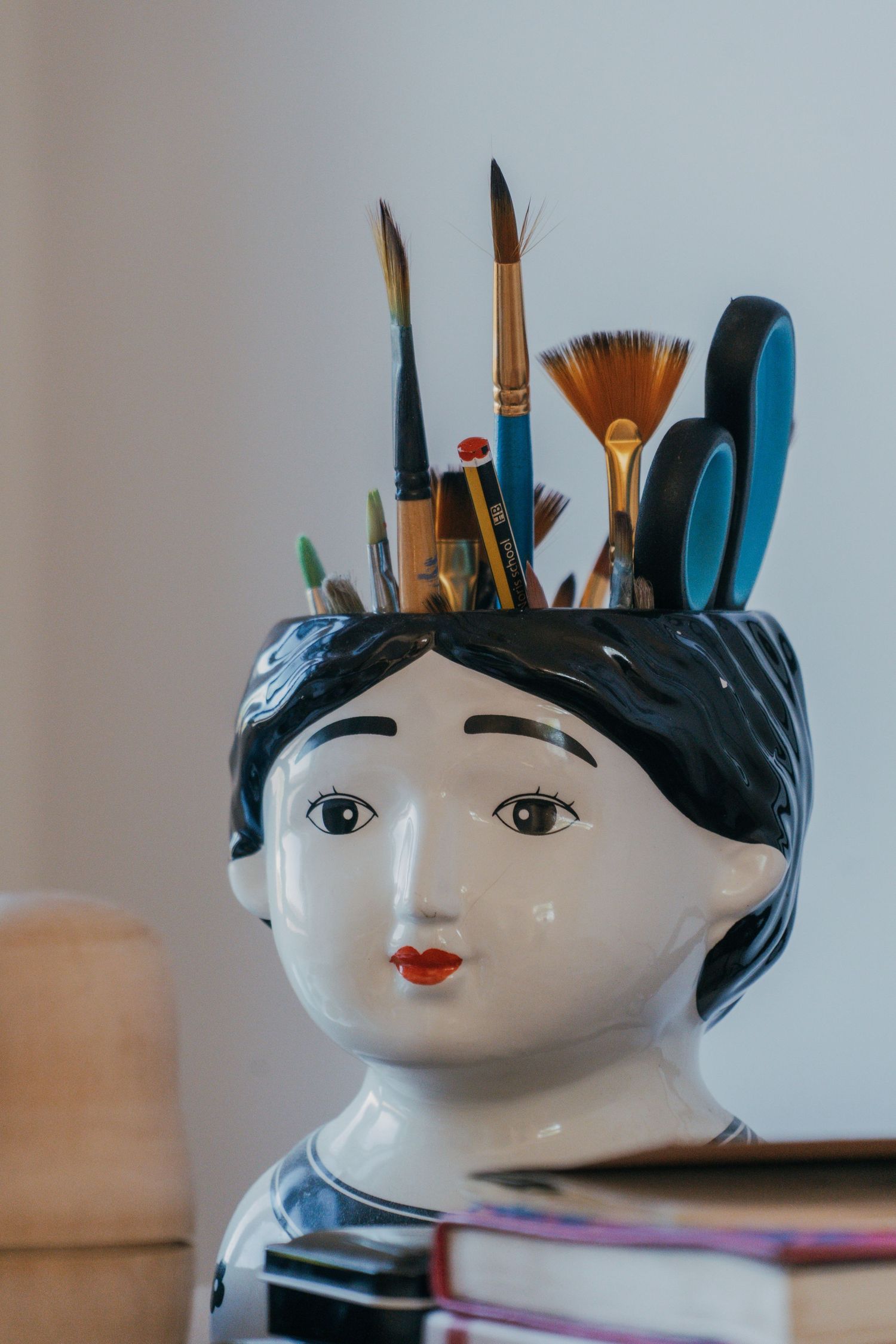 Decorative ceramic head planter with black hair and red lips holding art brushes and tools in creative workspace.