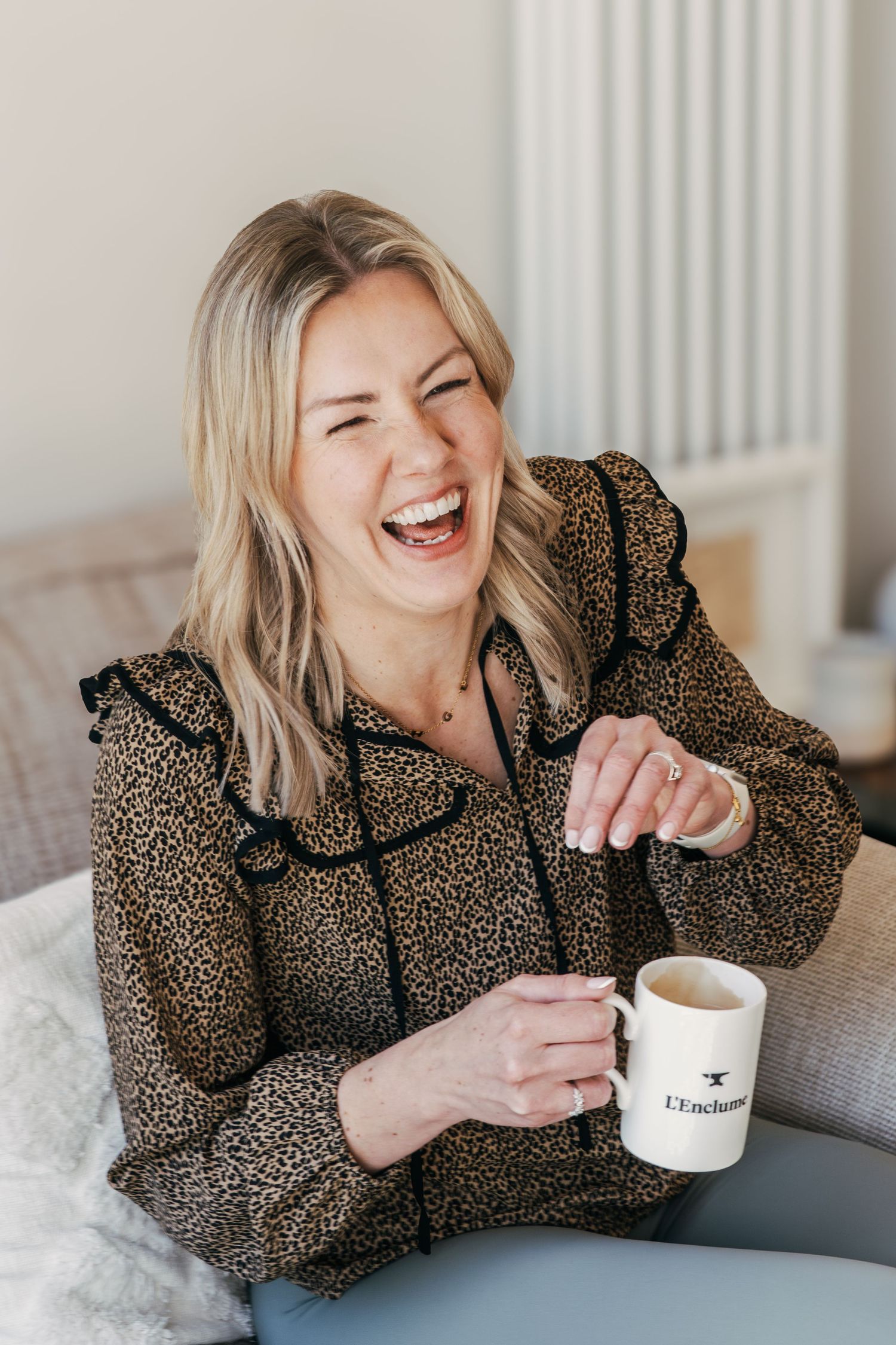 Person in leopard print blouse laughing joyfully while holding coffee cup.
