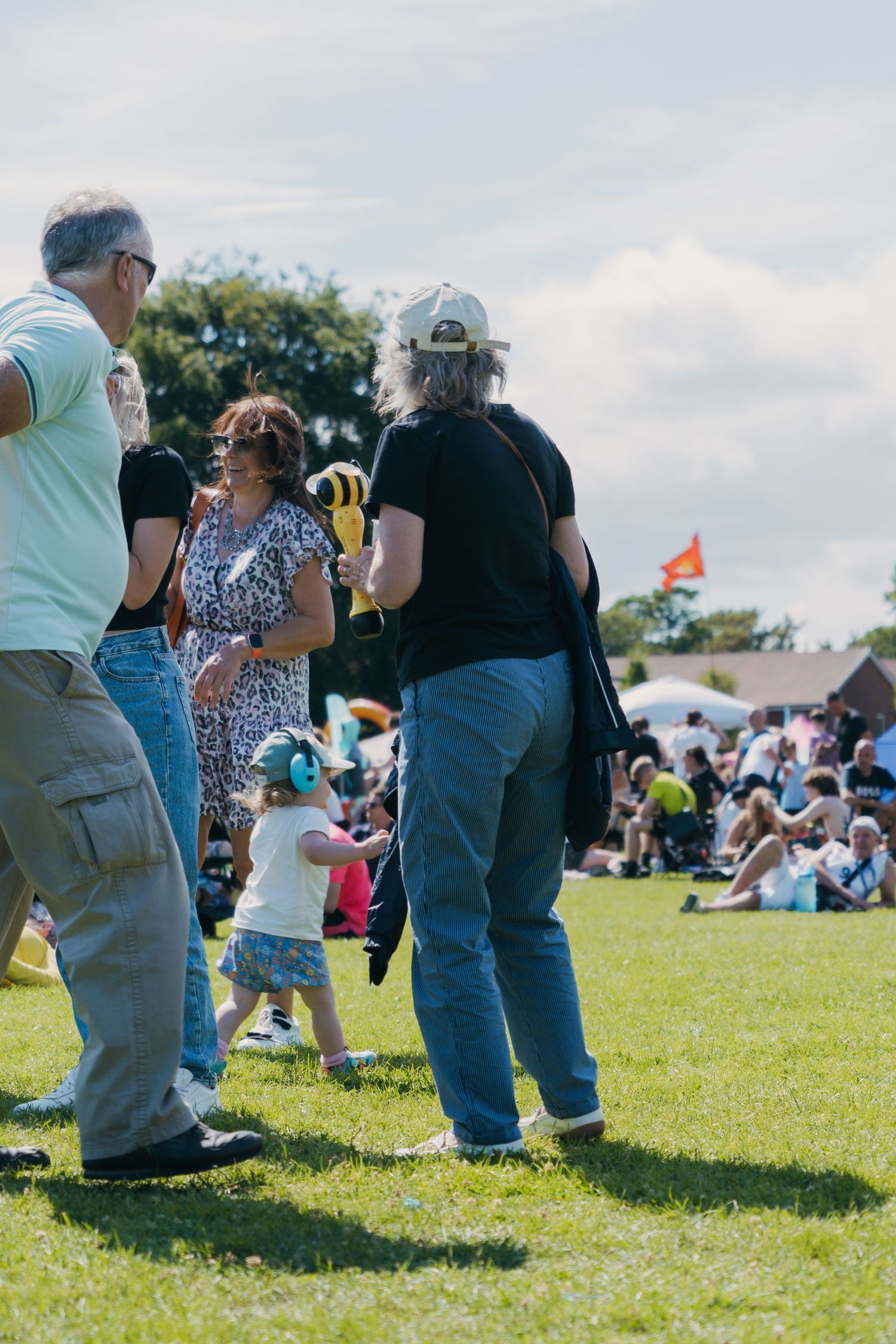 People sit and socialize on grassy lawn during an outdoor community gathering or festival on a sunny day.