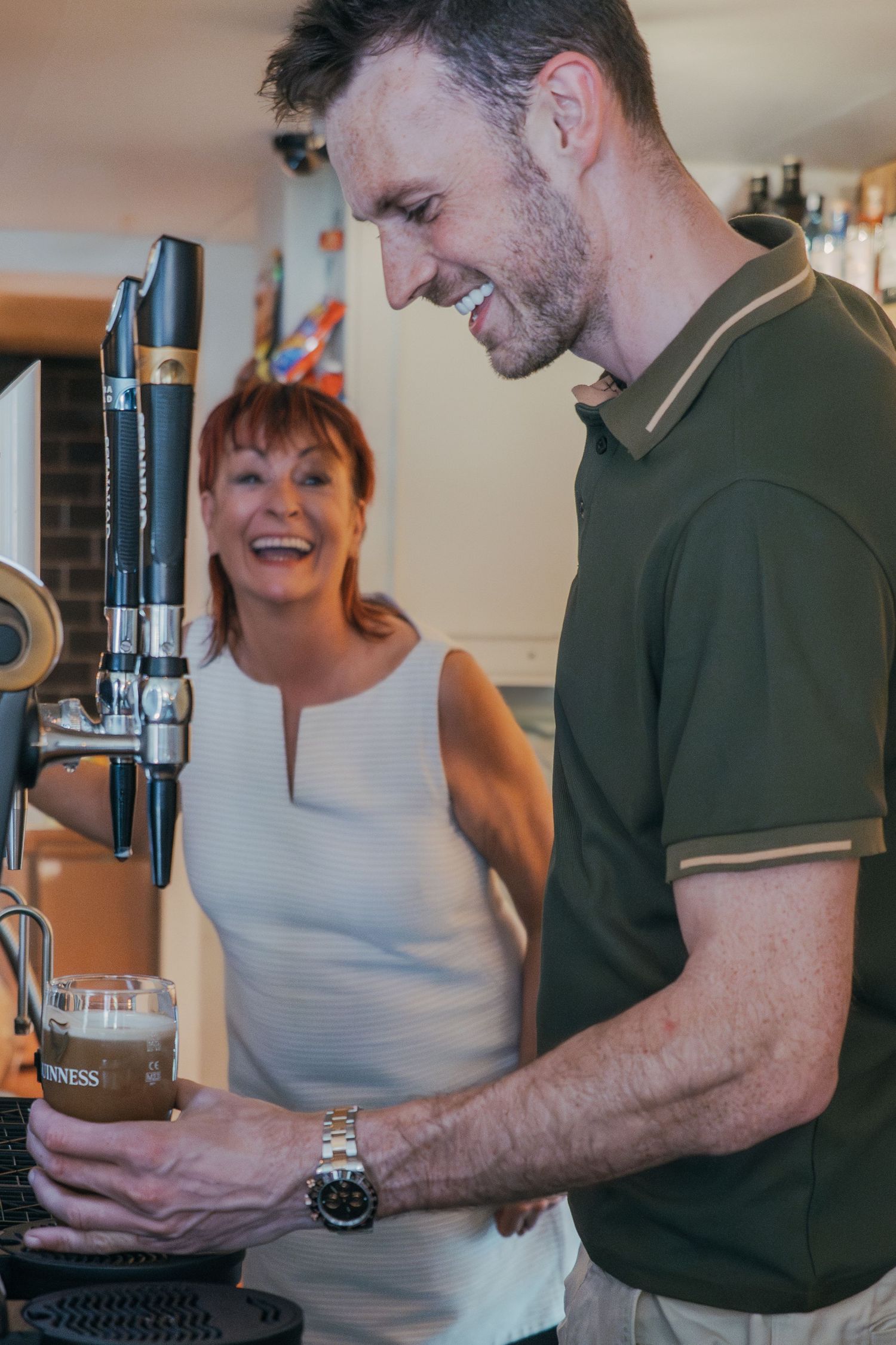 Brand Photography for bartenders. Two people sharing a laugh while pouring a draft beer from a tap system in a casual indoor setting.