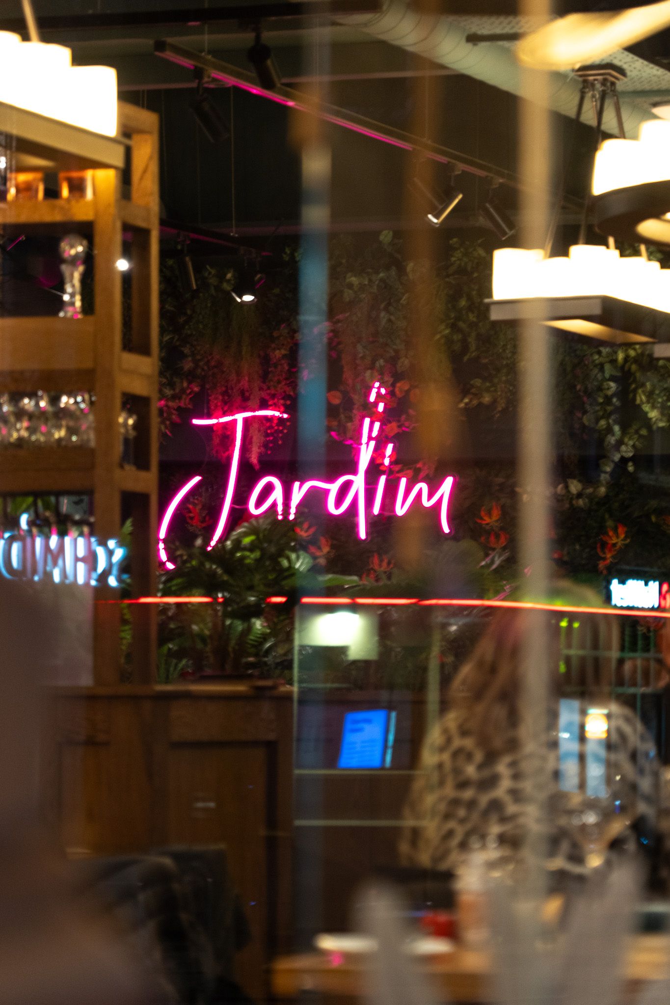 Pink neon sign reading 'Jardim' in cursive lettering inside restaurant.