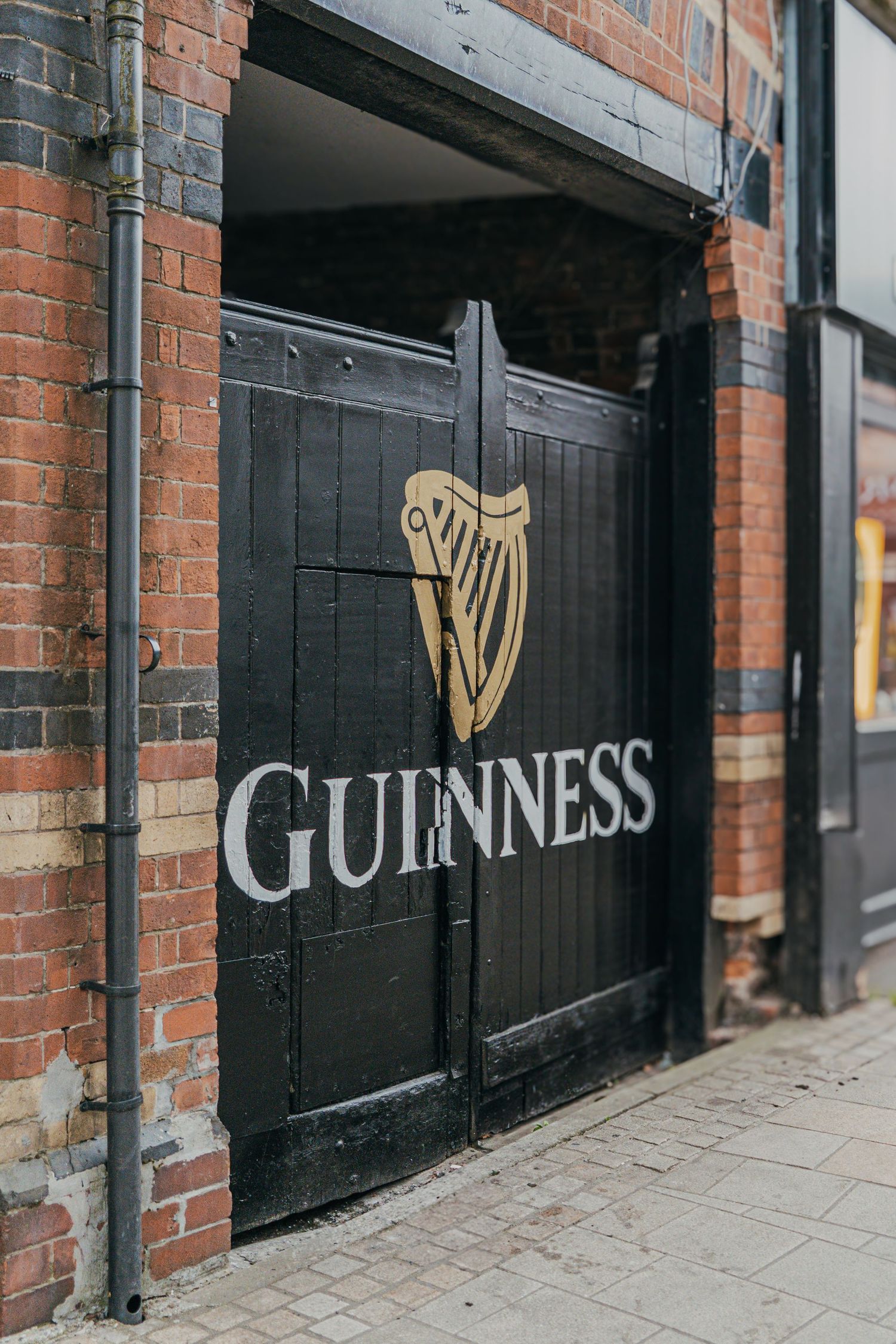 Black wooden doors with gold Guinness harp logo and lettering on red brick building exterior.