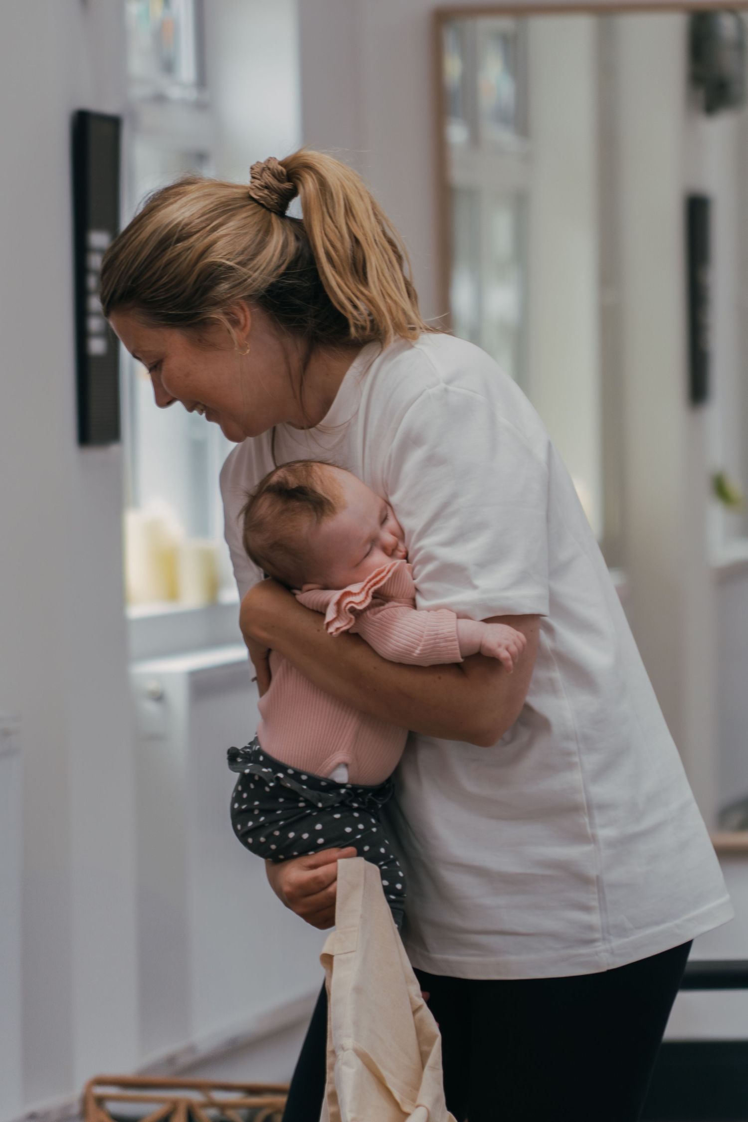 A tender embrace between parent and infant inside a bright interior room shows a sweet moment of connection and care.