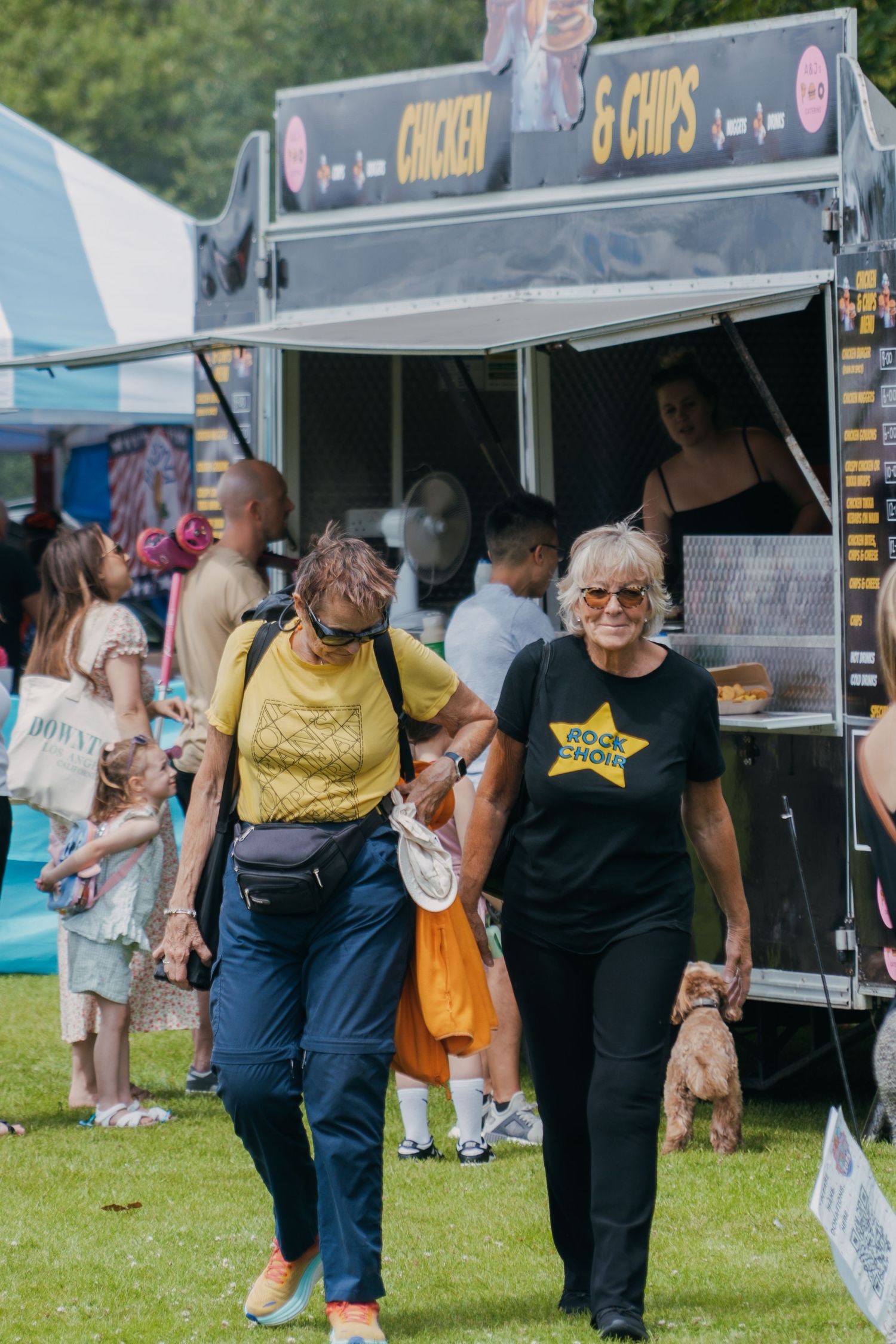People enjoying a summer food festival with food trucks and vendors on a grassy field outdoors.
