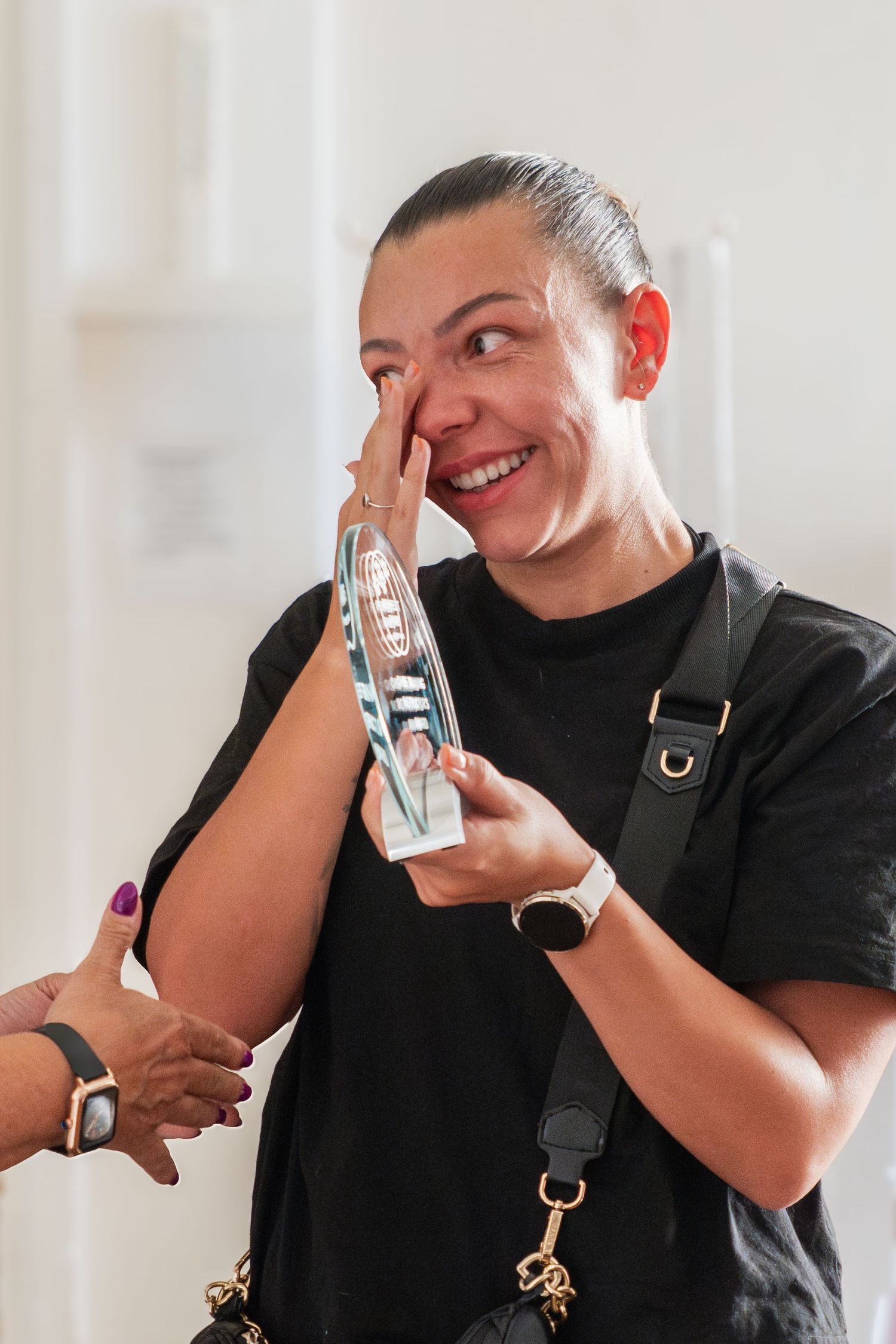 Person in black t-shirt laughing and holding a product with camera straps and smartwatch accessories.