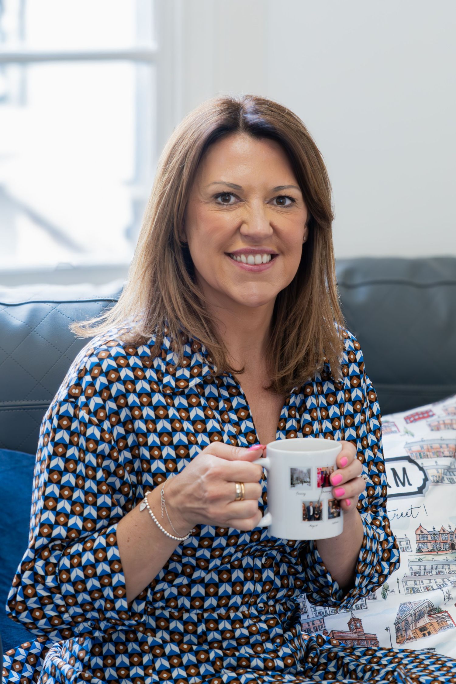 Someone relaxes on a couch holding a coffee mug while wearing a patterned blue and brown blouse.