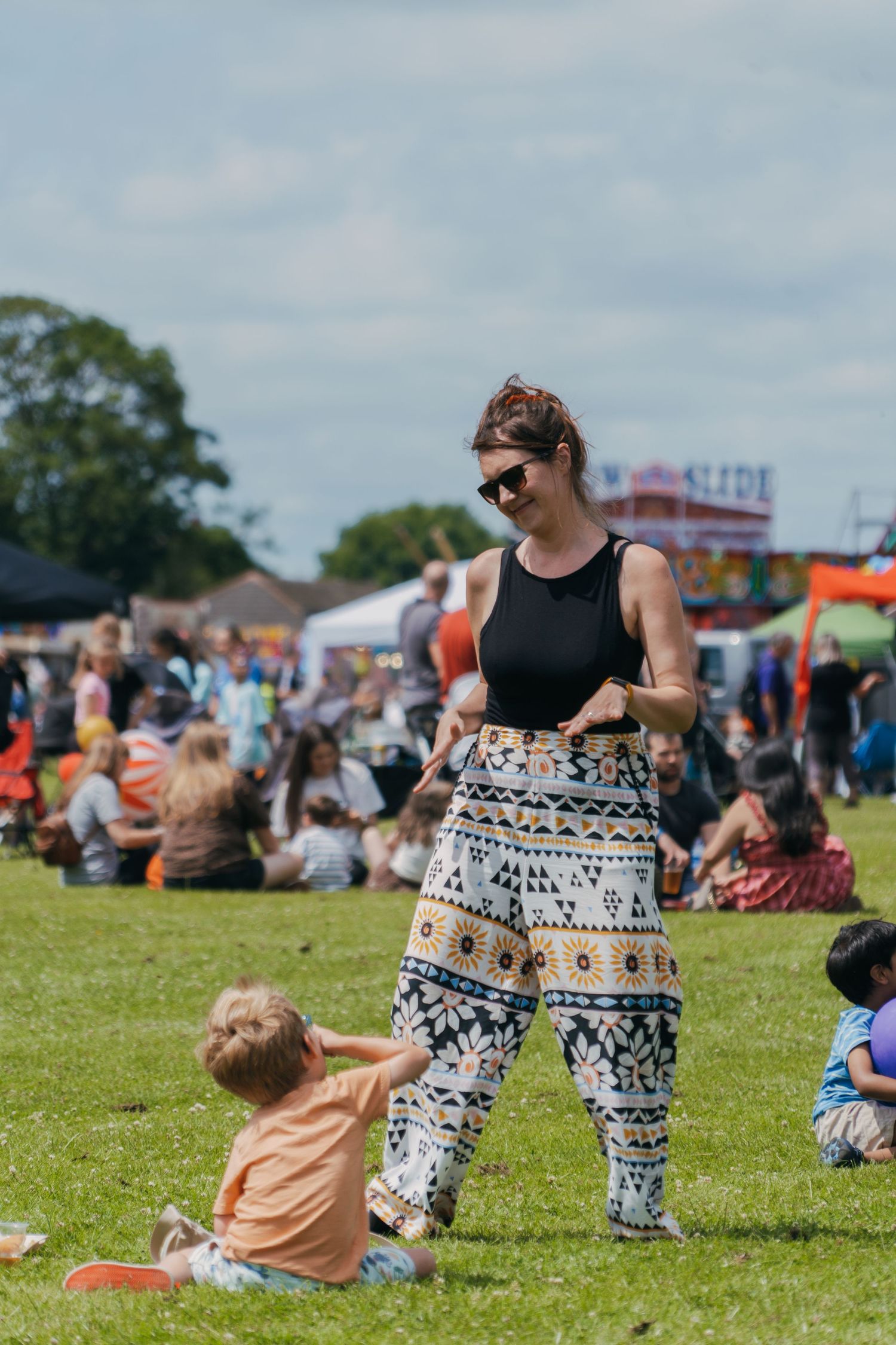 People enjoying a sunny outdoor festival with tents and activities on a grassy field.