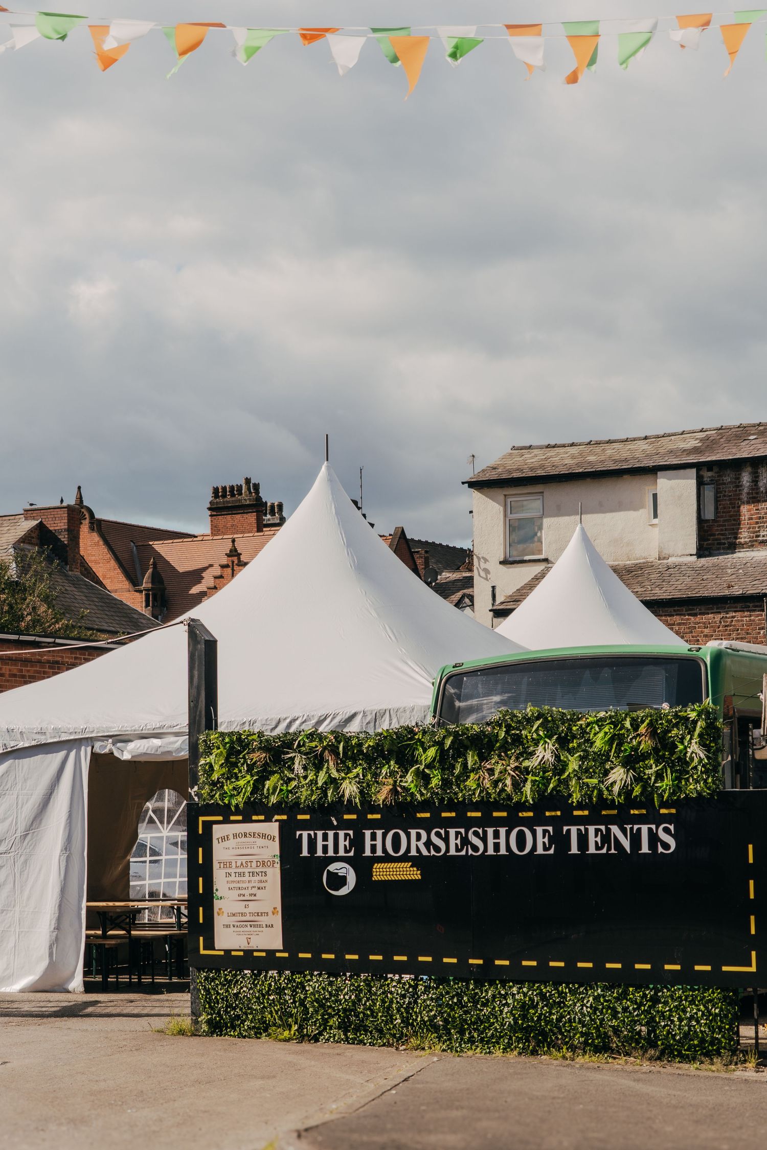 White event tents with 'The Horseshoe Tents' signage and decorative bunting flags against a cloudy sky.
