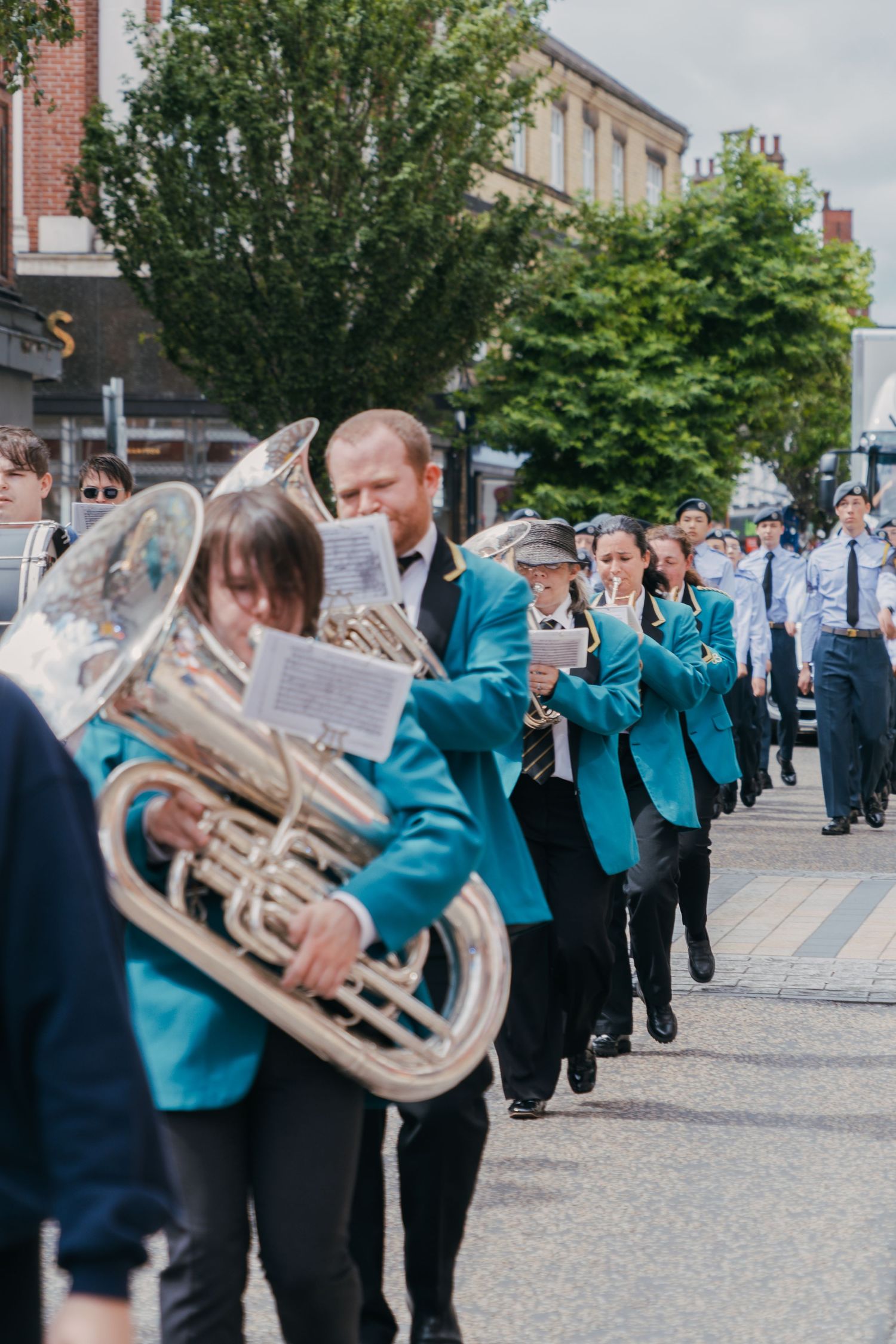 A marching band in turquoise uniforms performs while walking down a city street during a parade.
