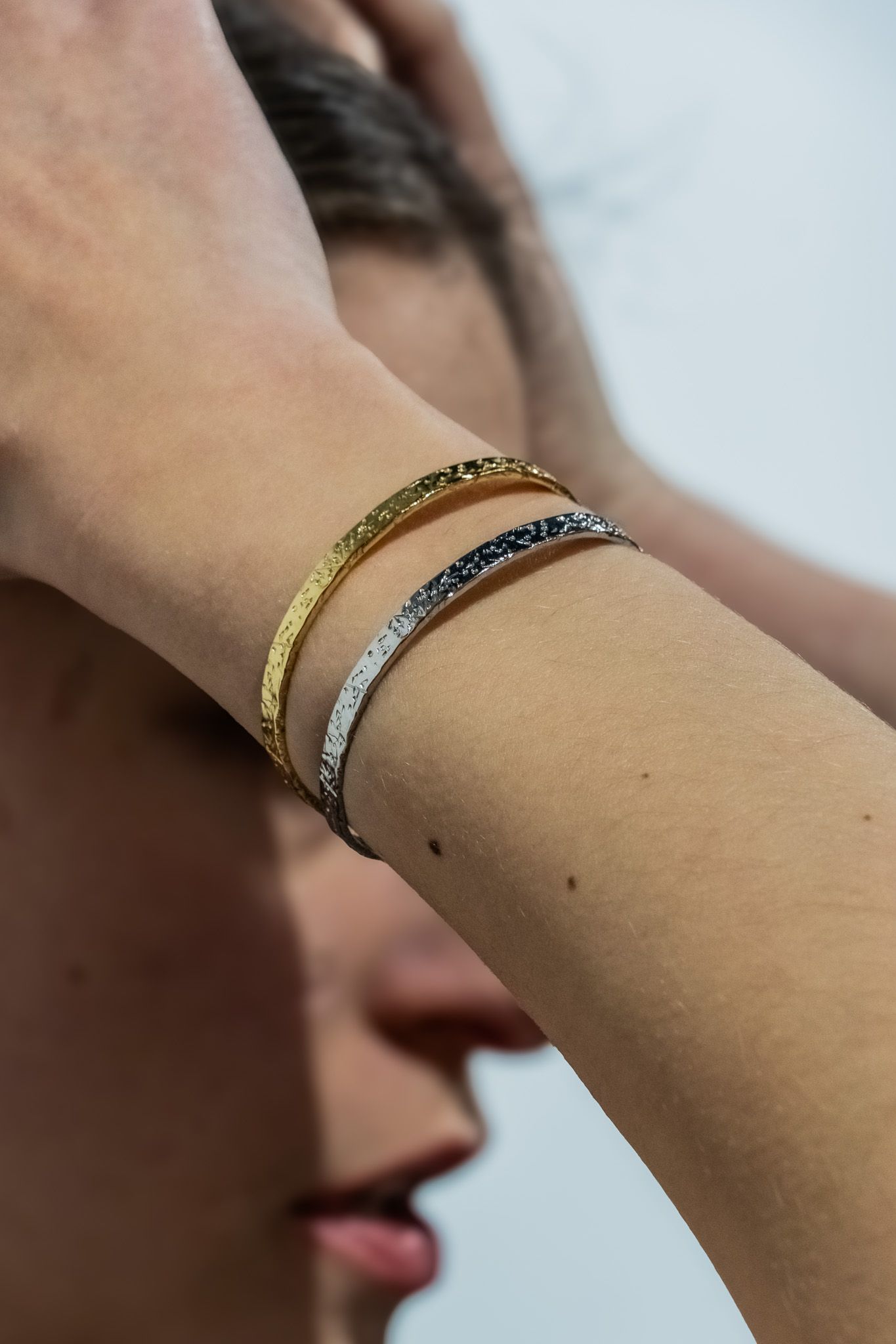 Close-up of gold and silver stacked bracelets worn on a wrist against a light background.