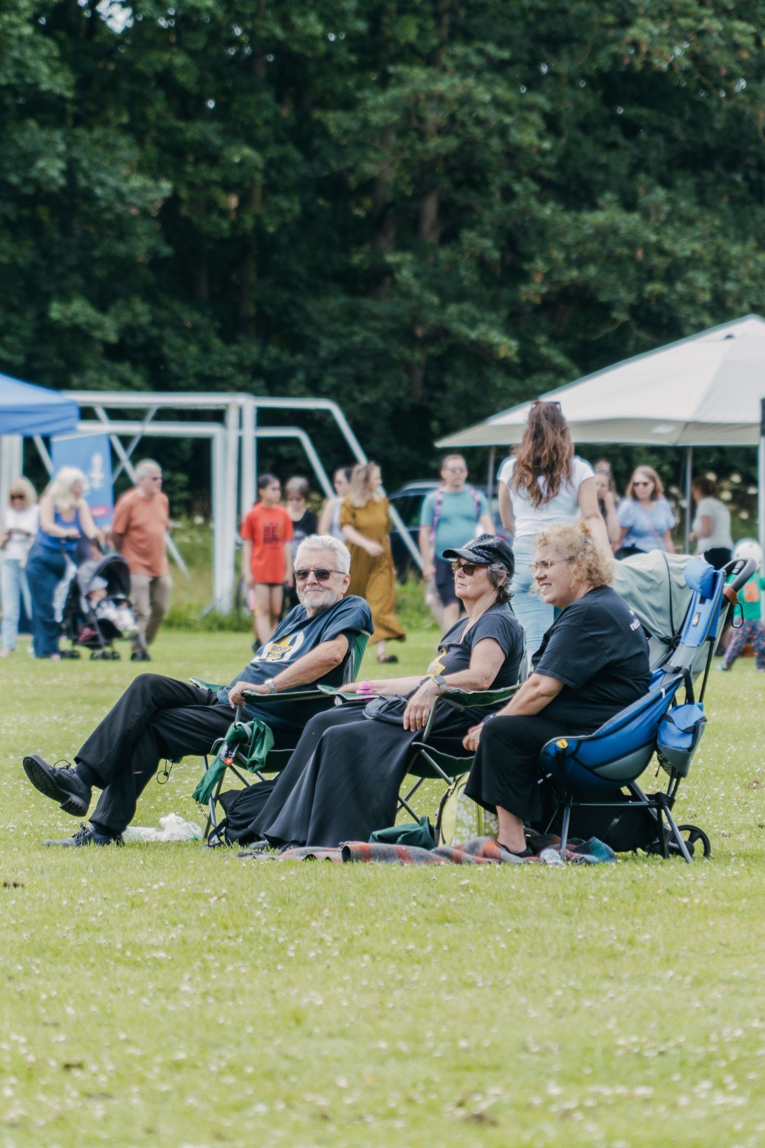 People sitting in camping chairs on a grassy field watching an outdoor event with tents in the background.