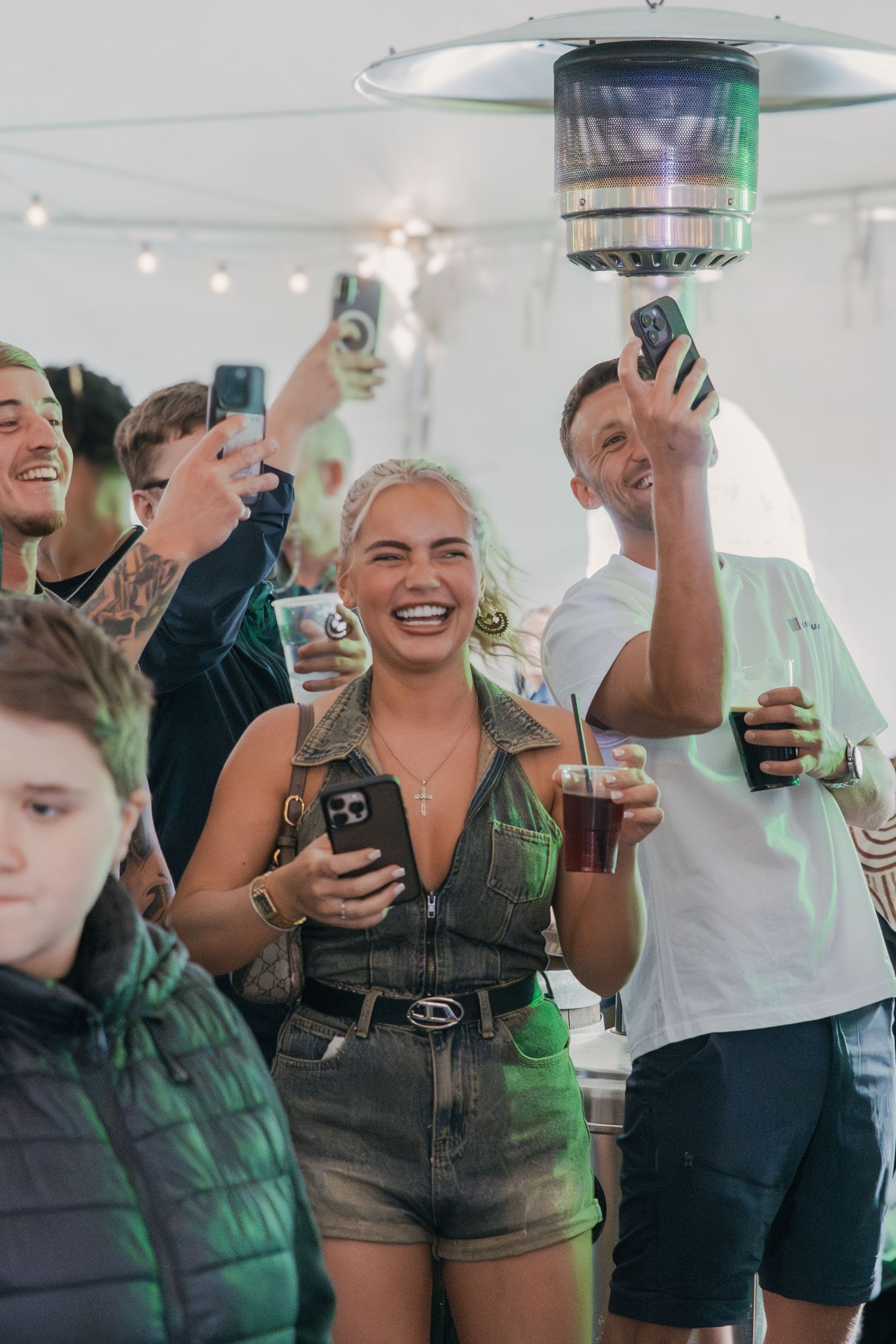 Group of partygoers enjoying drinks at a casual gathering with string lights overhead and phones in hand.