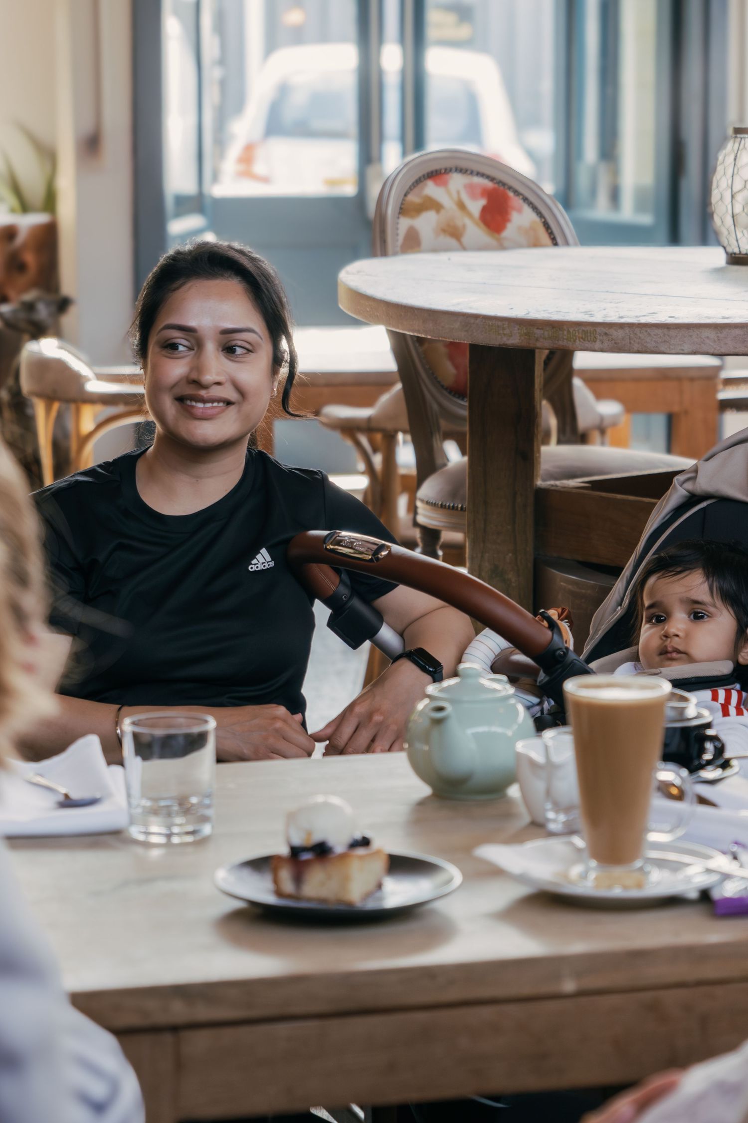A family enjoying beverages and dessert together at a cafe with a wooden table and teapot setting.