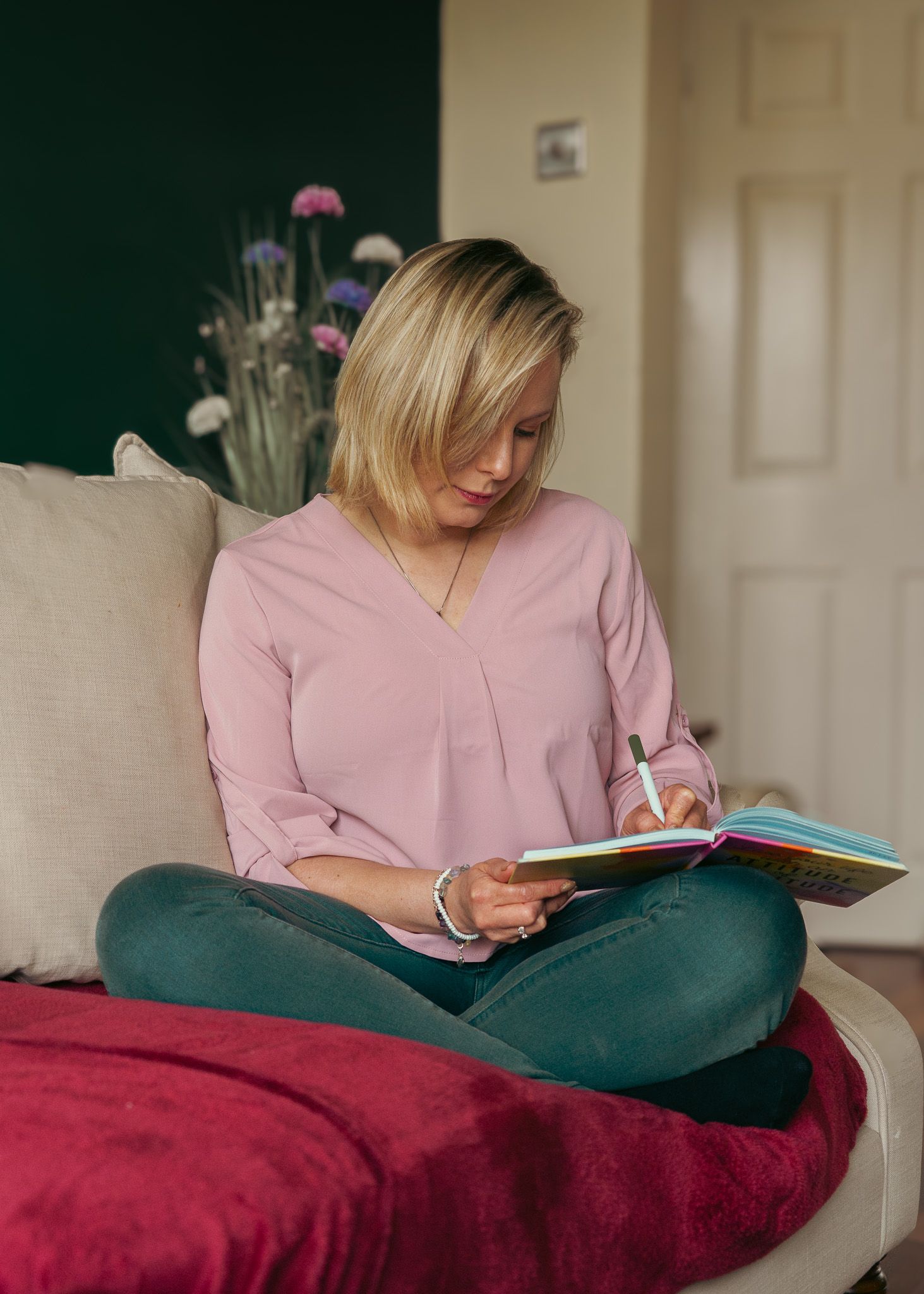 Person in pink top reading book while sitting on red cushion.