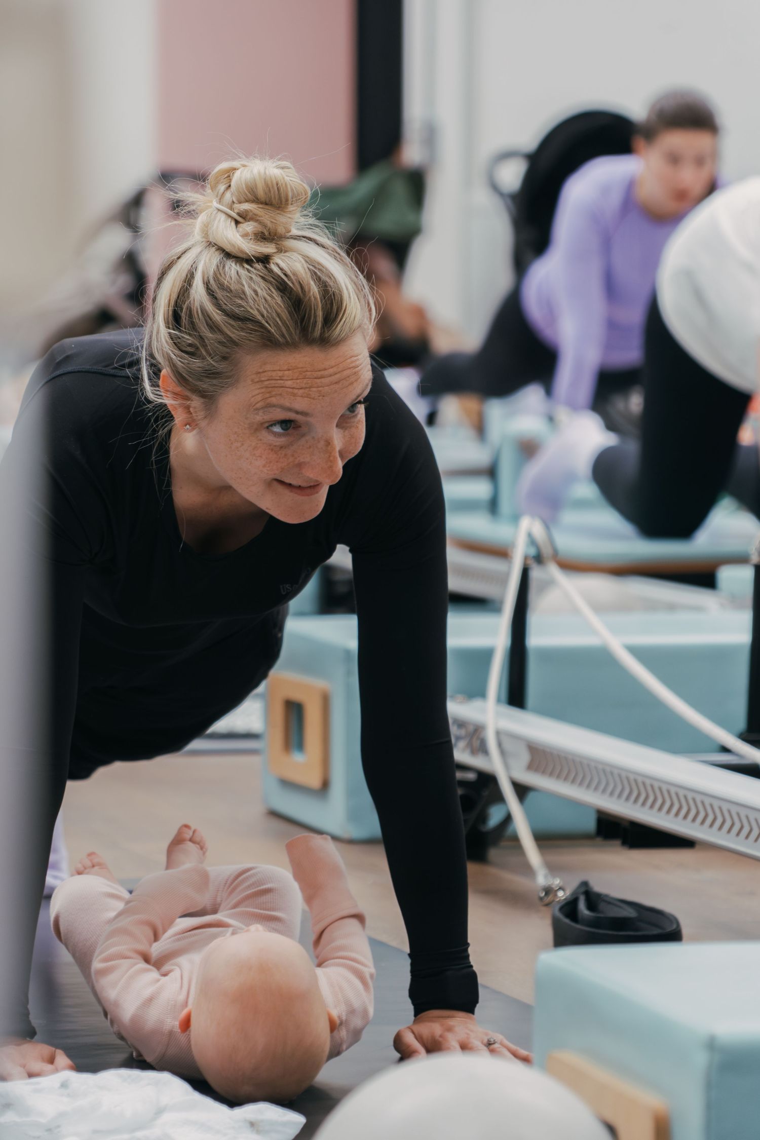 Mother and baby sharing a moment during a fitness class with workout equipment in the background.
