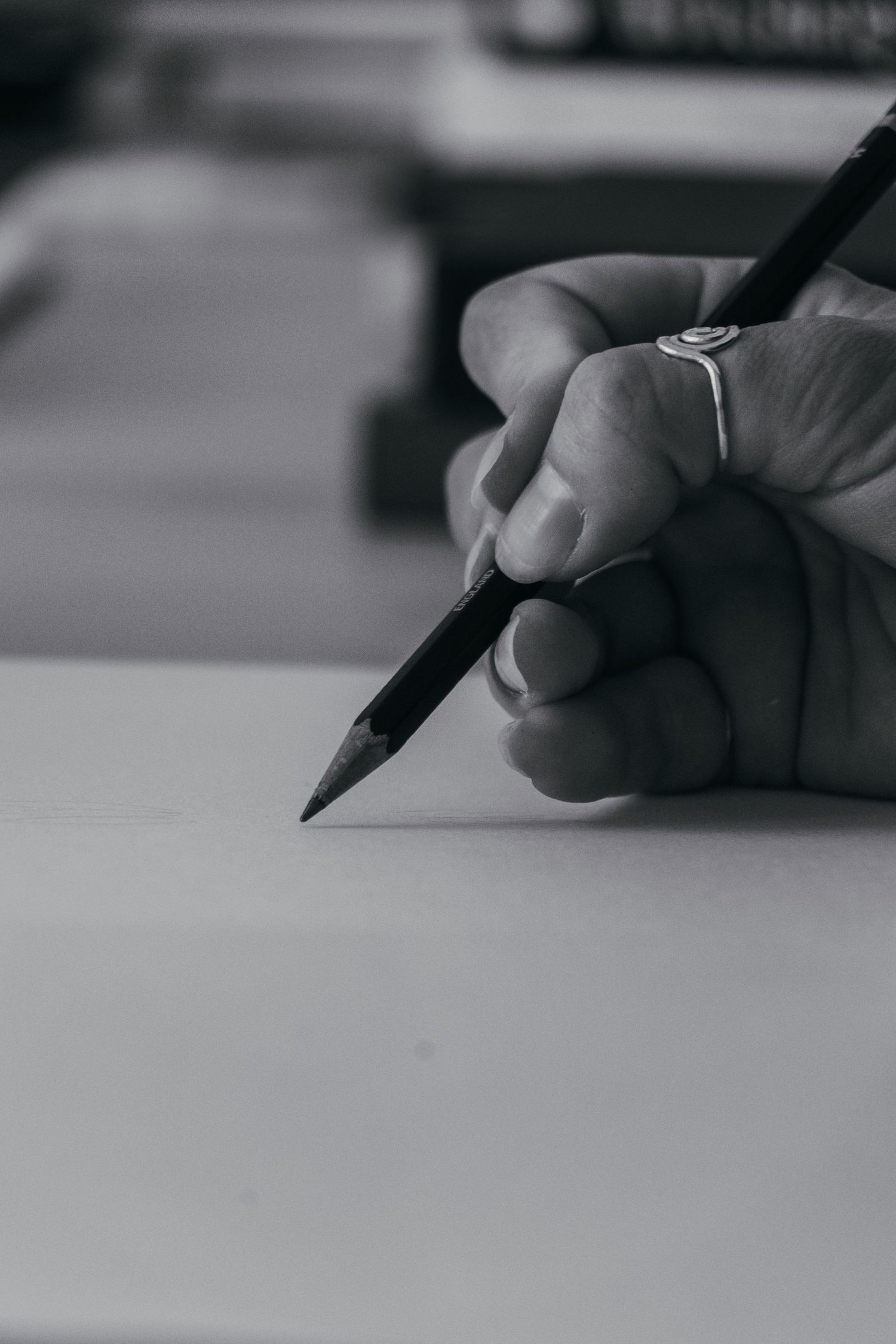Close-up black and white photo of hand holding pencil poised to write on blank white paper.