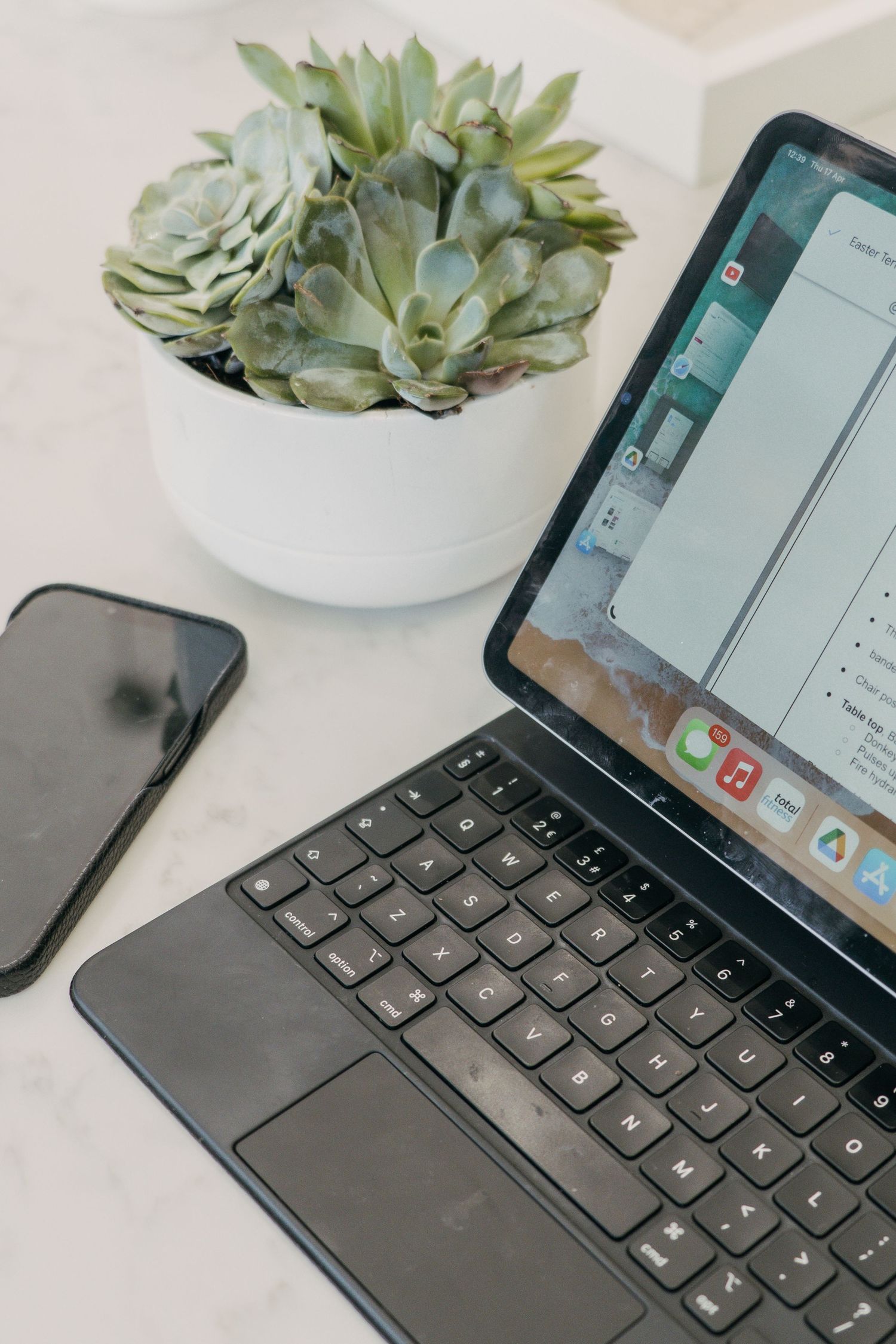 iPad with wireless keyboard and succulent plant on white desk showing sleek modern workspace setup.