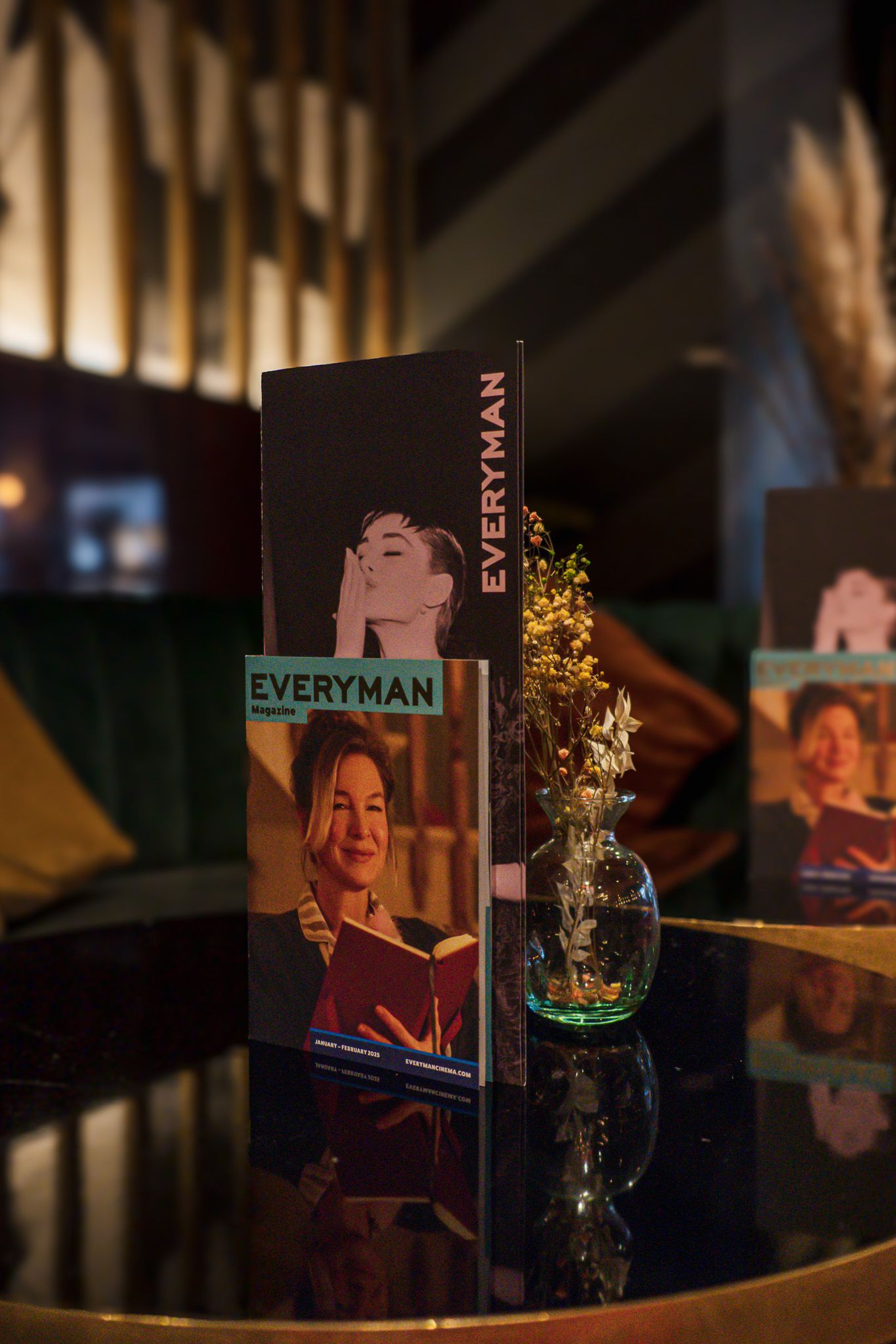 Advertising materials displayed in a dark setting with a small vase of dried flowers.