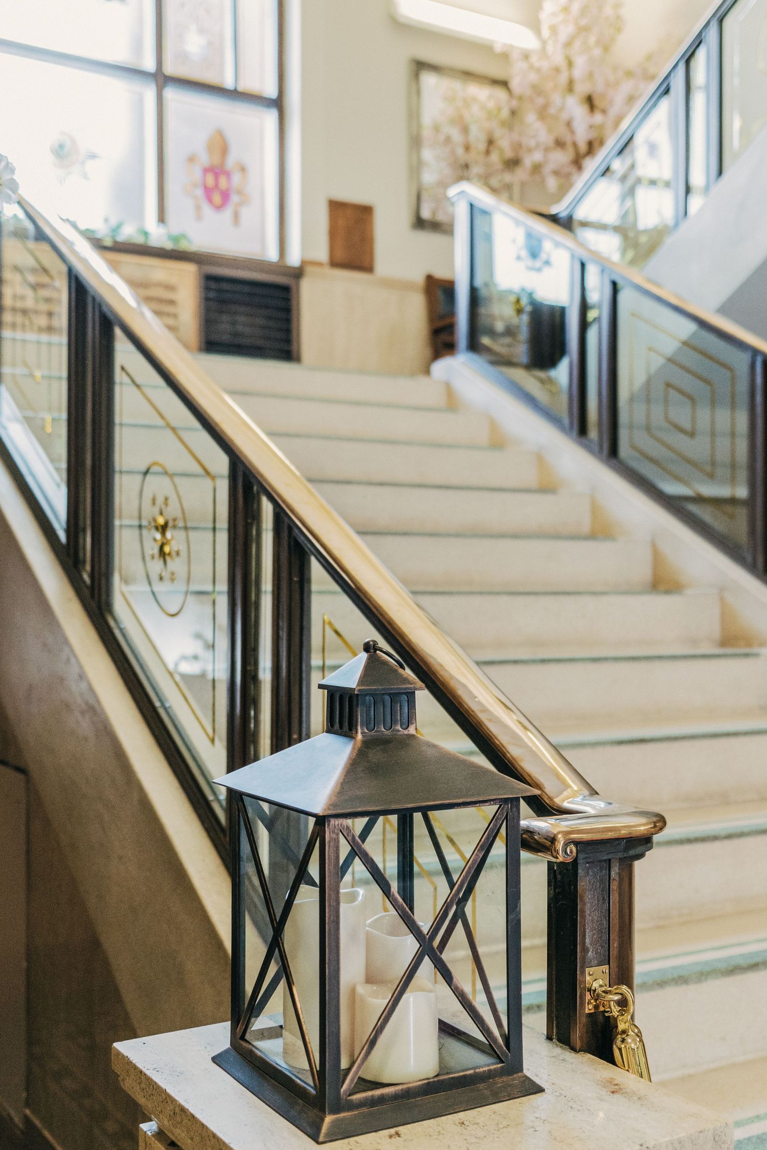 Black metal lantern decorates elegant white staircase with glass panels and wooden handrails in bright interior space.