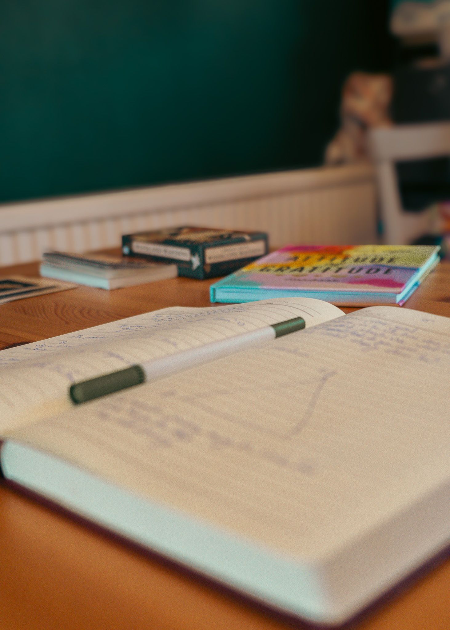 Open notebook with pen and colorful books on a wooden desk surface.