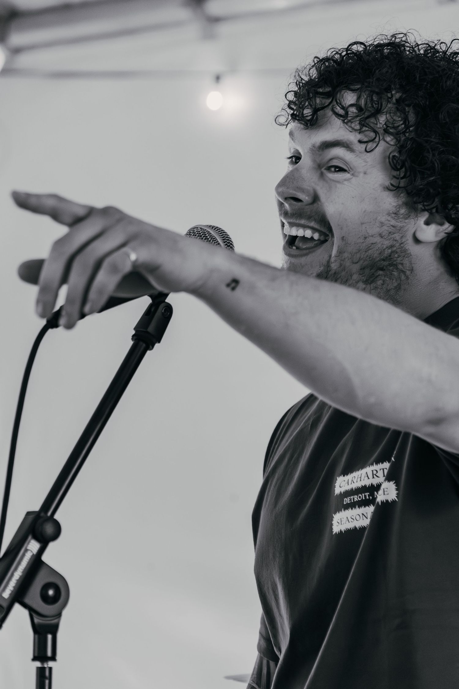 A vocalist with curly hair performing on stage points energetically while singing into a microphone.
