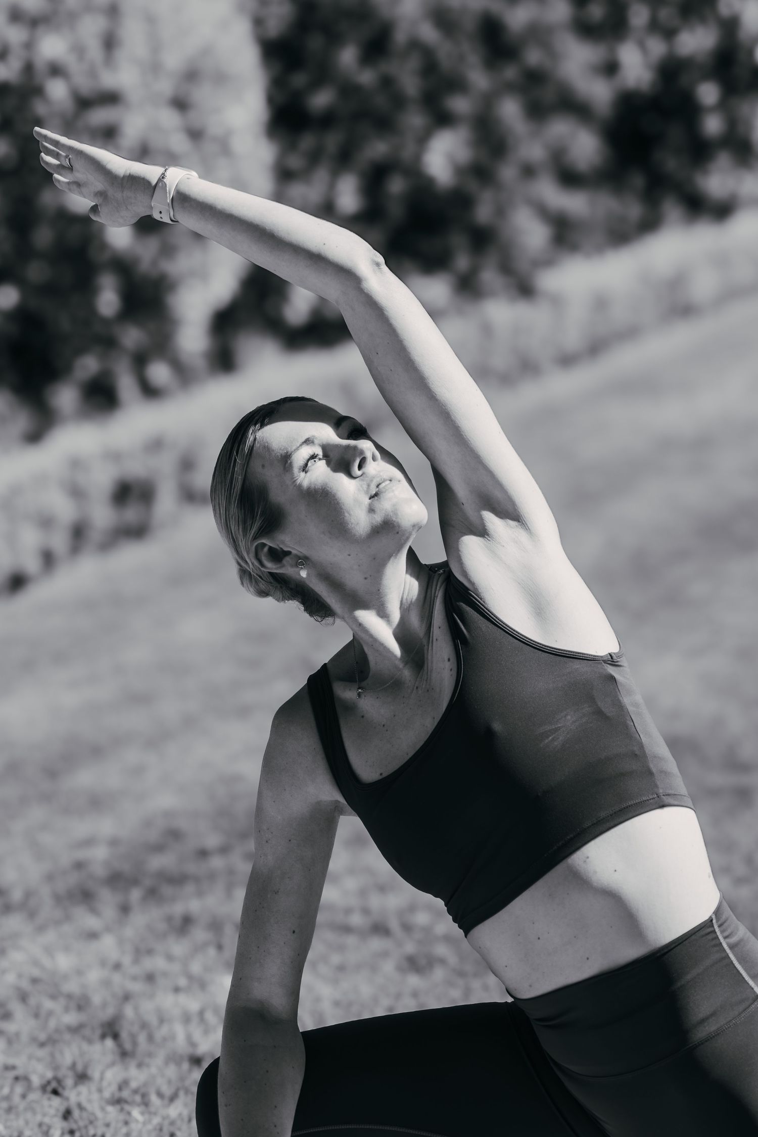 A black and white photo of someone stretching in yoga attire outdoors, performing a side bend exercise.
