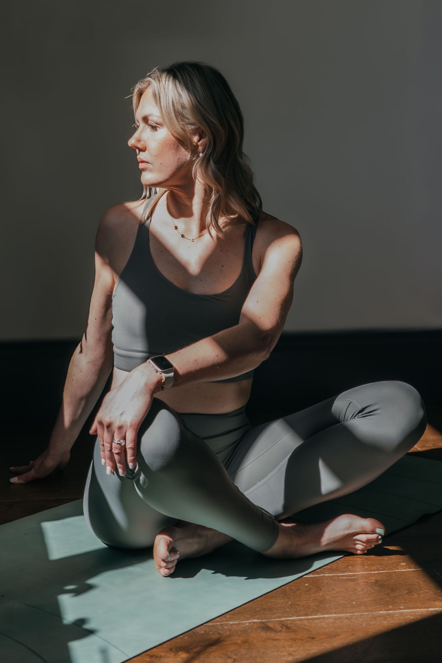 Athletic woman in workout attire stretches on yoga mat in moody studio lighting.