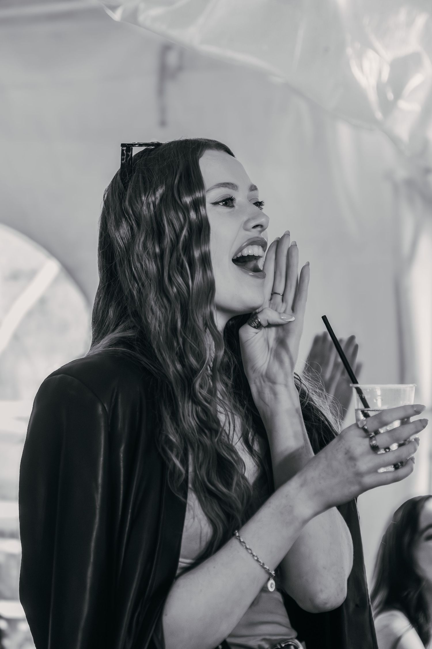A person in black laughing joyfully while holding a drink at a social gathering, captured in black and white.