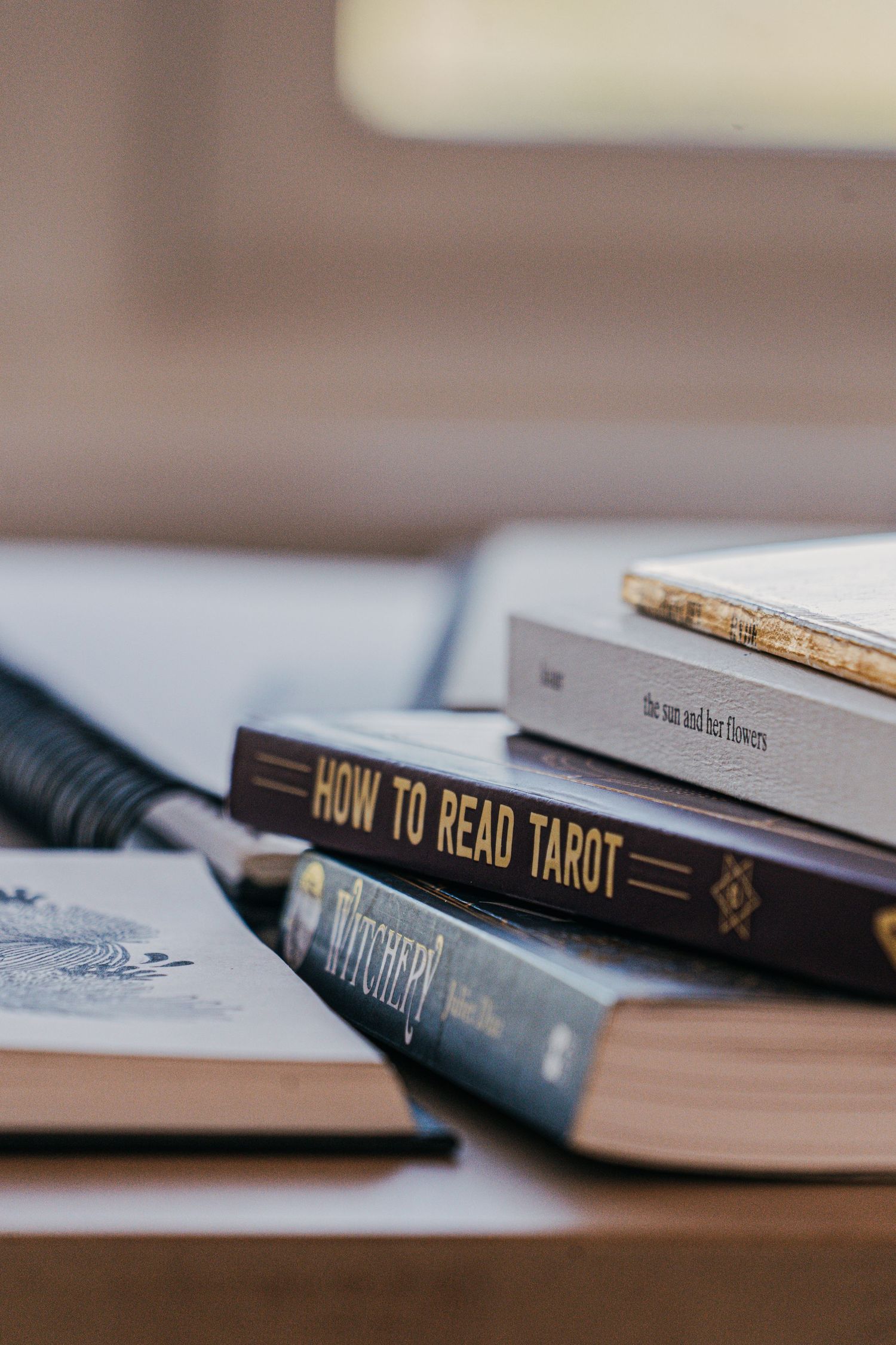 A stack of books on spiritual topics including 'How to Read Tarot' along with writing materials on a wooden surface.
