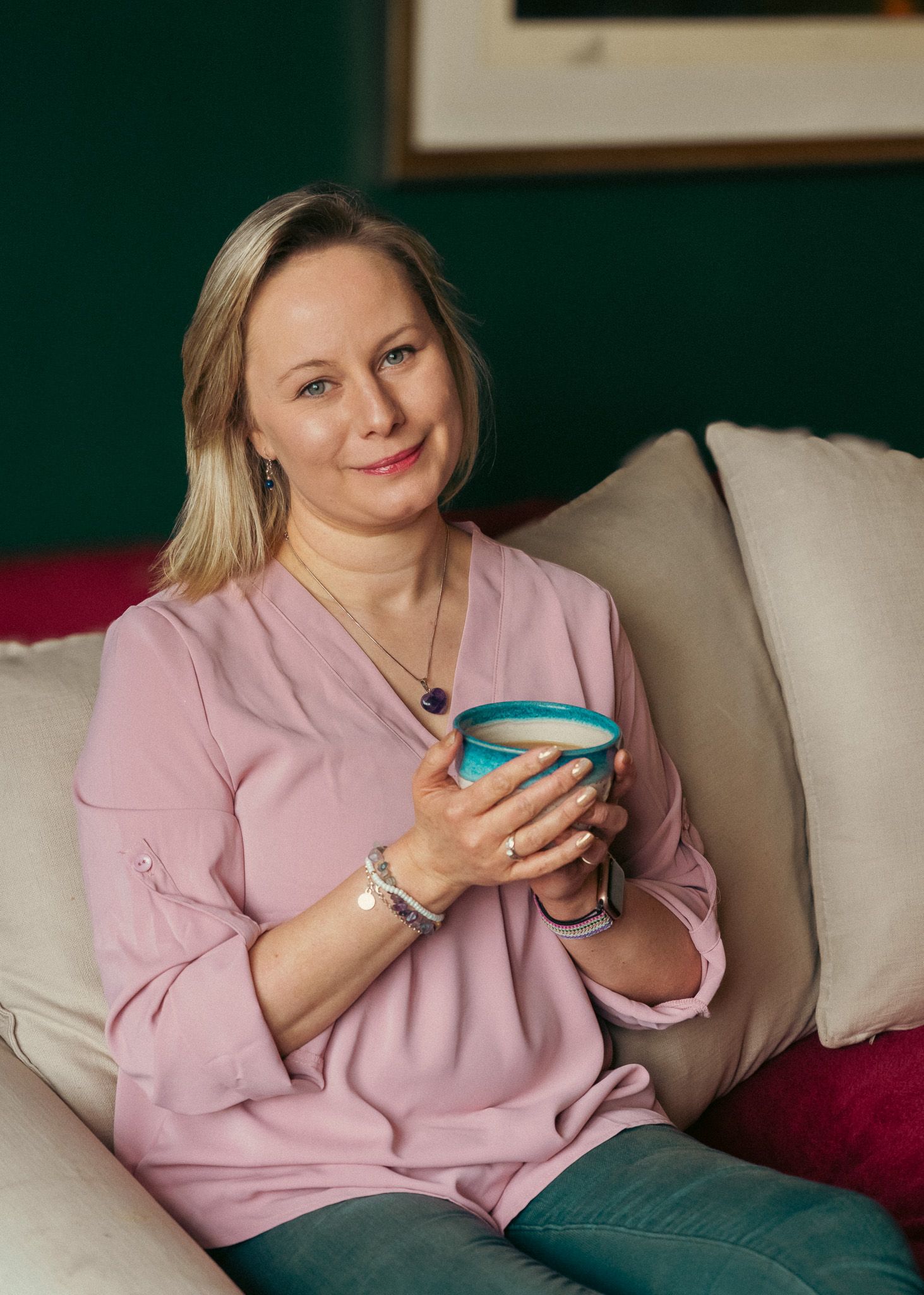 Person in pink blouse relaxing on beige couch with turquoise mug.