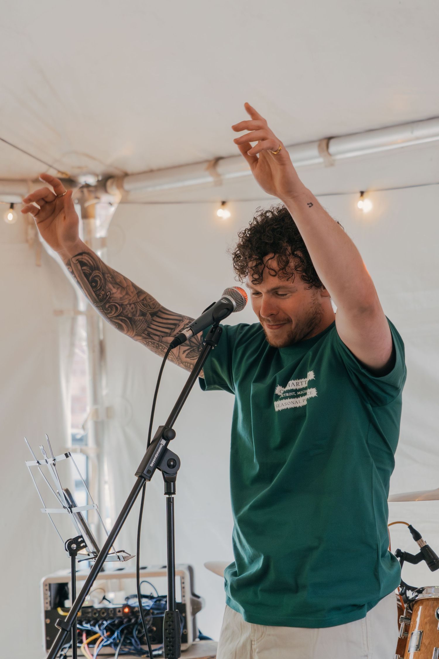 An energetic performer in a green t-shirt raises their arms while singing into a microphone during a live performance.